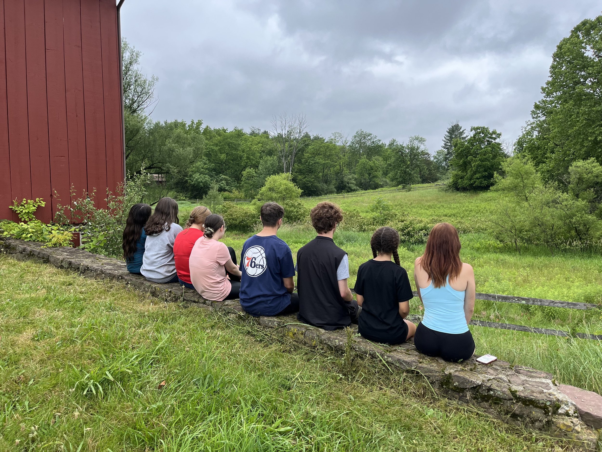 Youth sitting on a stone wall along a field next to a red barn