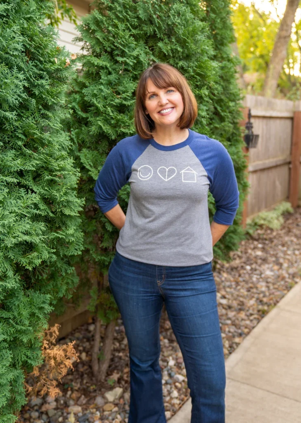 Professional organizer from Happy Healthy Home in Des Moines smiling in a branded baseball tee outdoors.