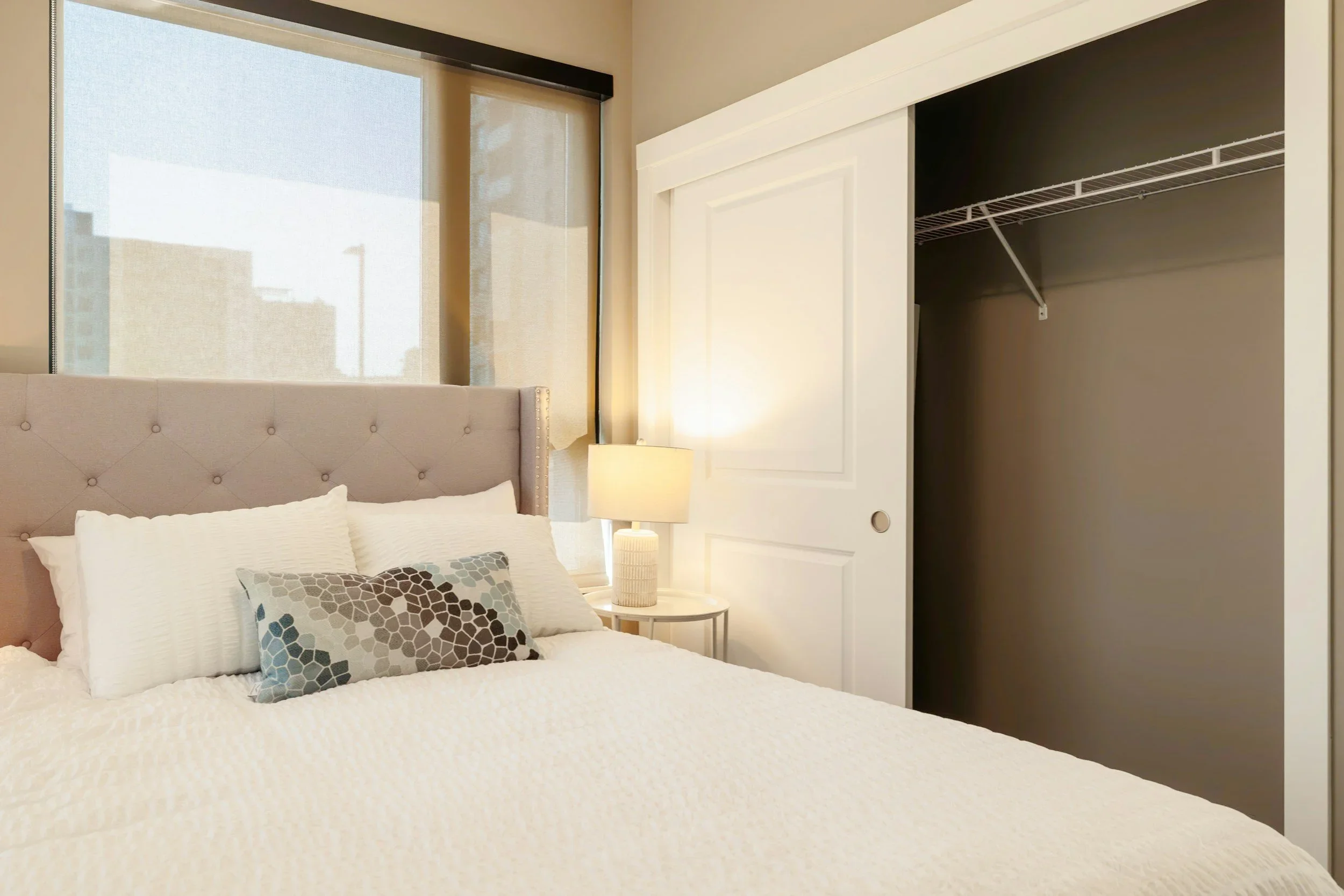 Professional bedroom and closet organization by Home By Eleven in Minneapolis, featuring a tufted headboard and a clean reach-in closet.