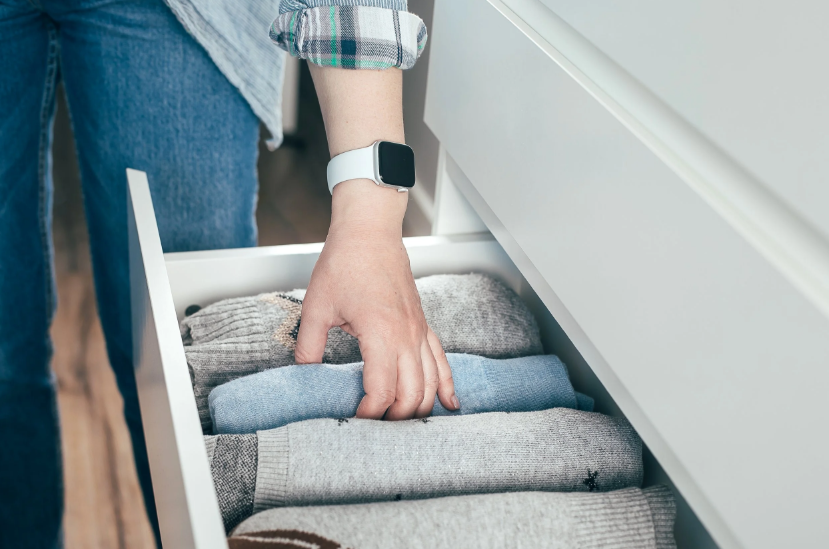 A professional organizer from Pro Organizer Studio vertically folding sweaters into a white dresser drawer.