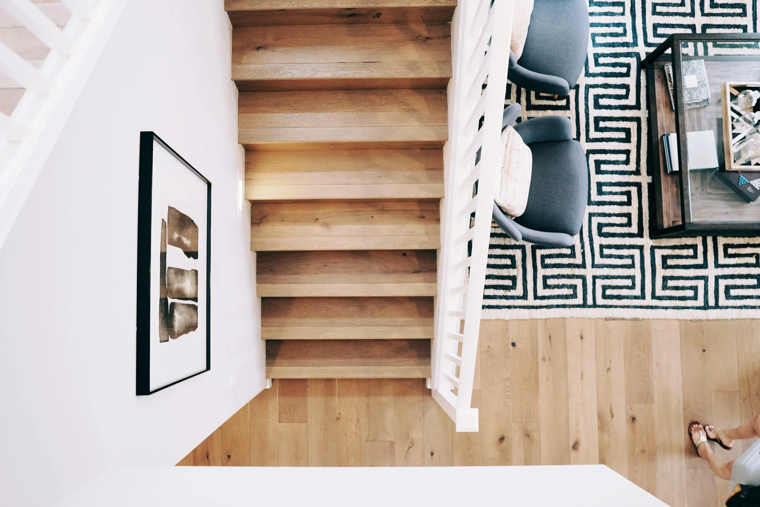 Overhead view of a modern home with blonde wood stairs, a white minimalist interior, and a geometric rug in Los Angeles.
