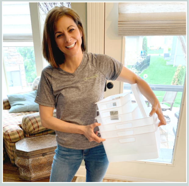 Professional organizer Karen Swart of Organizing-Etc. holding a stack of clear storage bins for a home organization project in Kansas City.