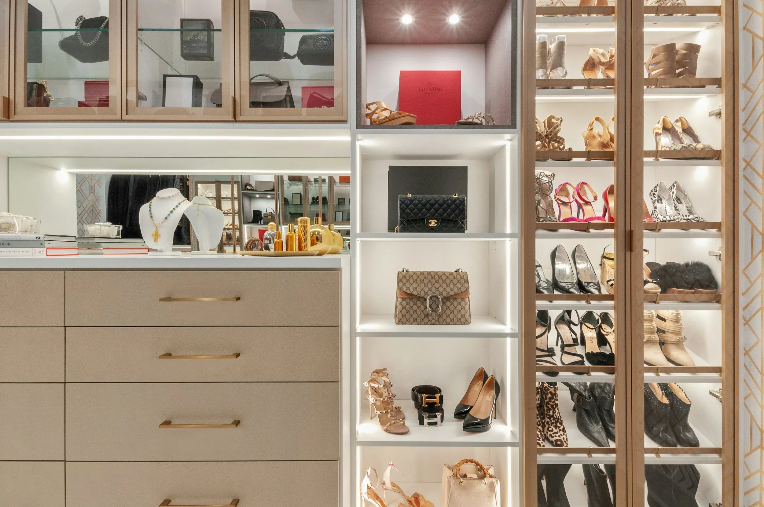 A luxury custom closet by Function Forward Lifestyle featuring illuminated shelves for designer handbags and shoes.