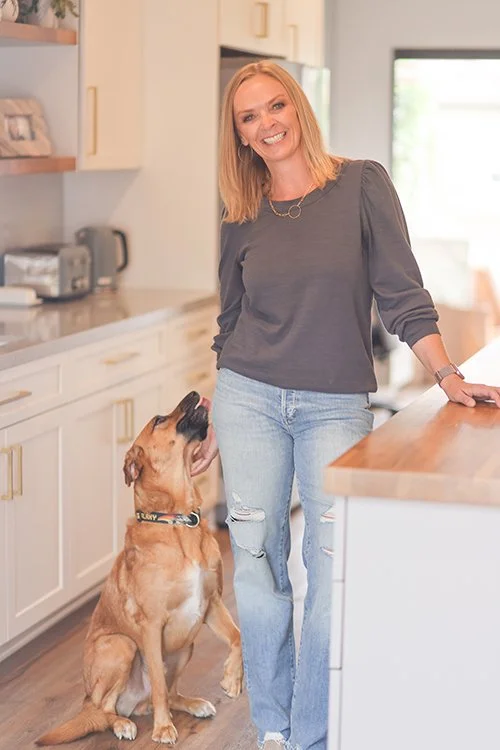 Kimberly of North County Concierge smiling with a tan dog in a bright, modern kitchen.