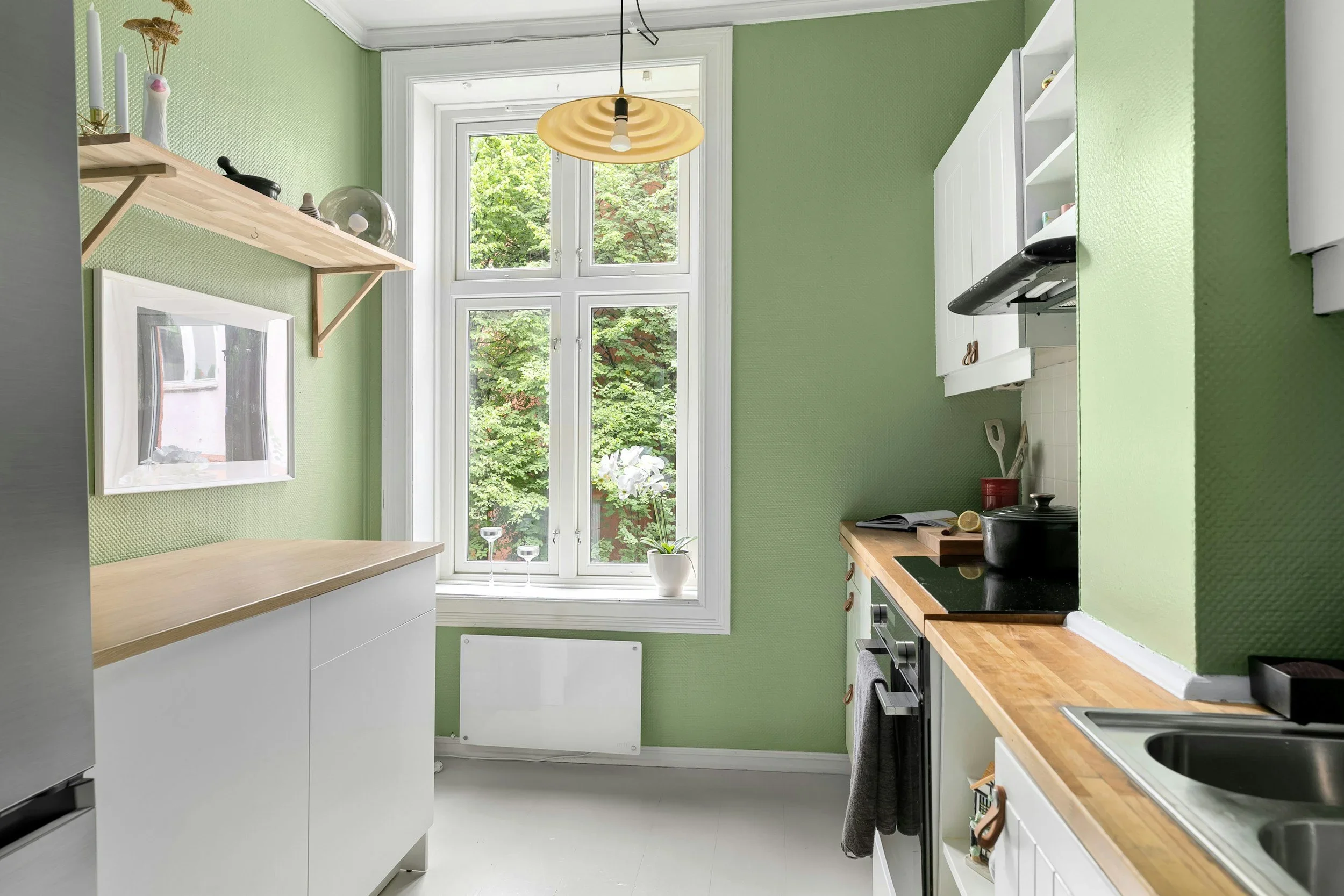 Bright, organized kitchen with sage green walls, white cabinets, and natural wood countertops.