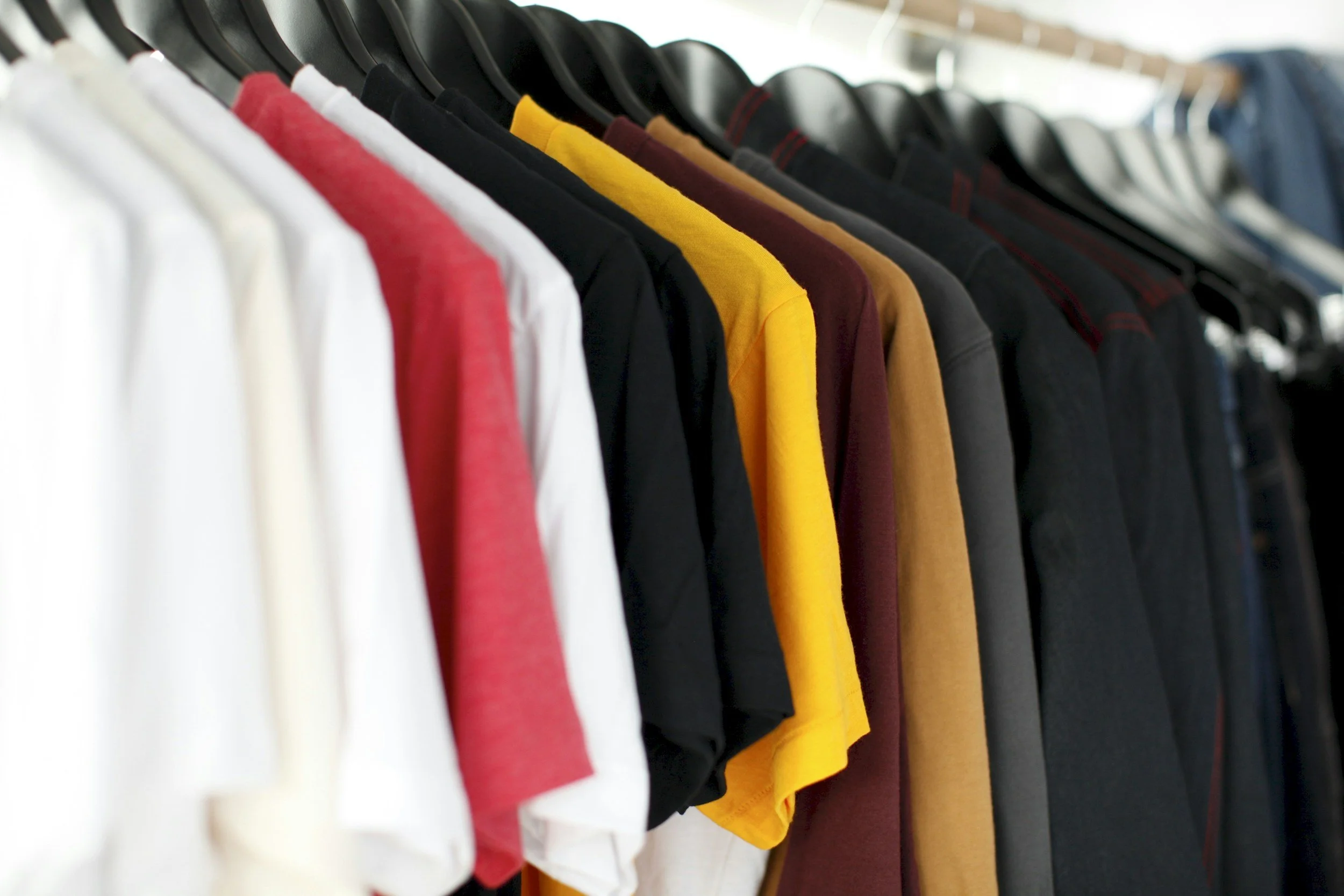 A row of various colored shirts and t-shirts hanging neatly on black hangers.