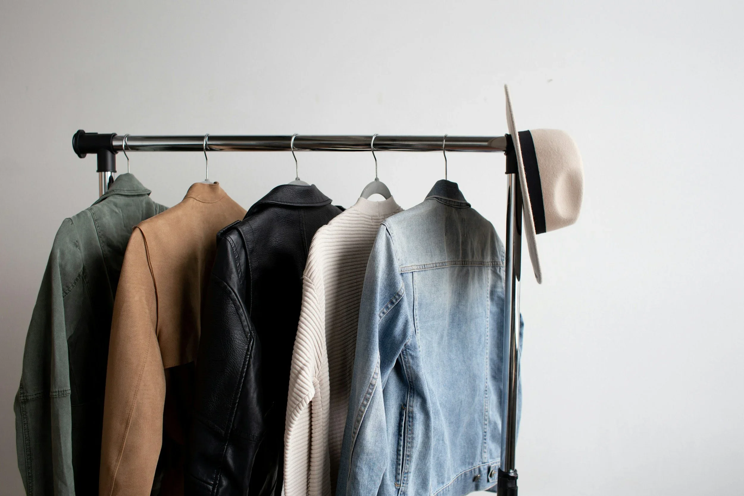 A minimalist clothing rack by Pretty and Practical featuring a denim jacket, leather jacket, and wide-brimmed hat.