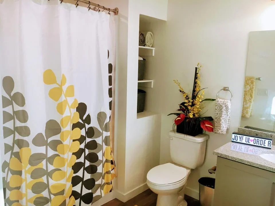Bright organized bathroom with a yellow floral shower curtain and recessed shelving for storage.