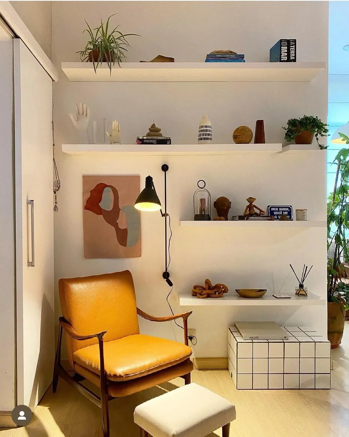 Modern reading nook with an orange leather armchair, floating white shelves, and curated decor.