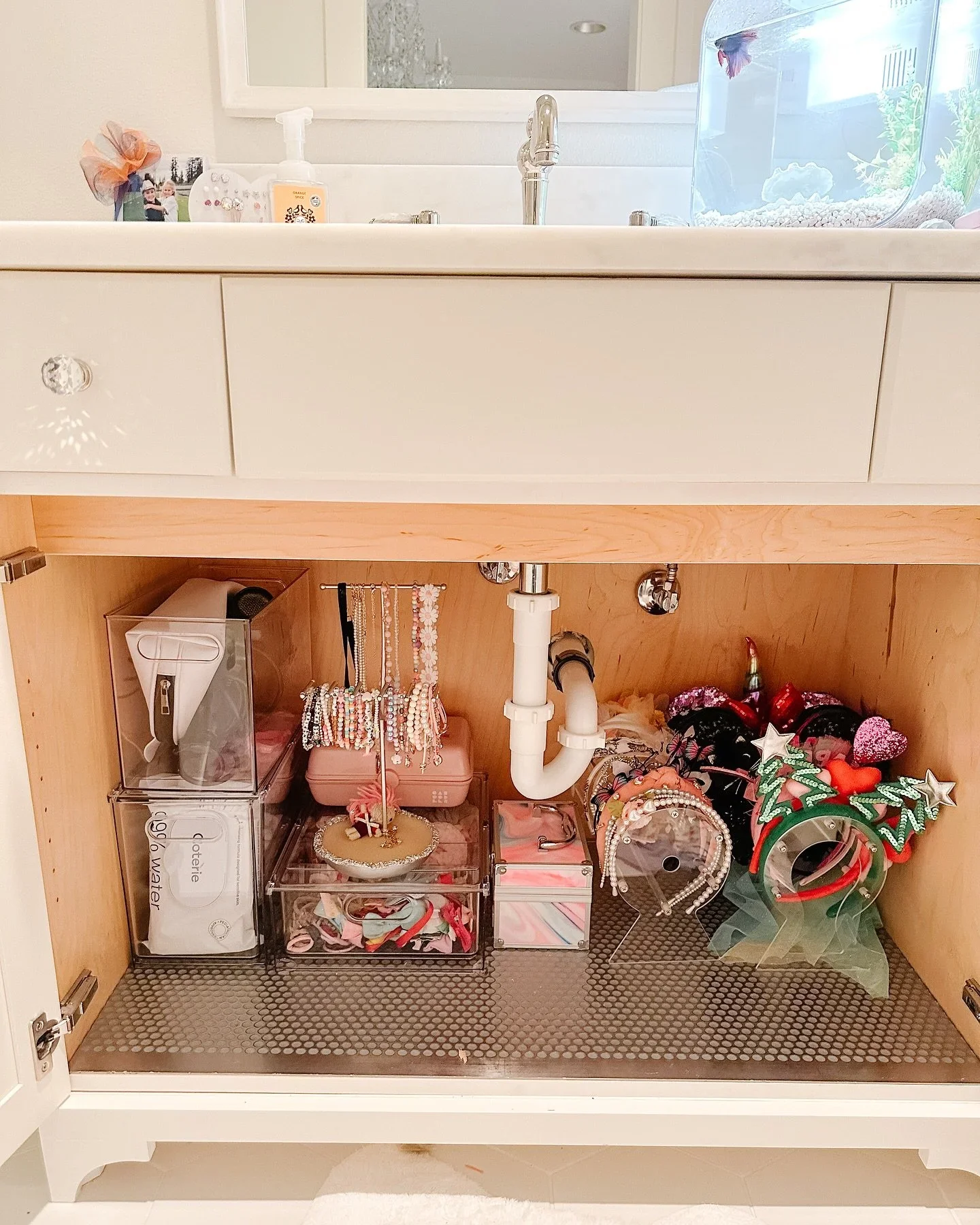 Organized bathroom cabinet with clear stackable bins, jewelry stands, and colorful headbands.