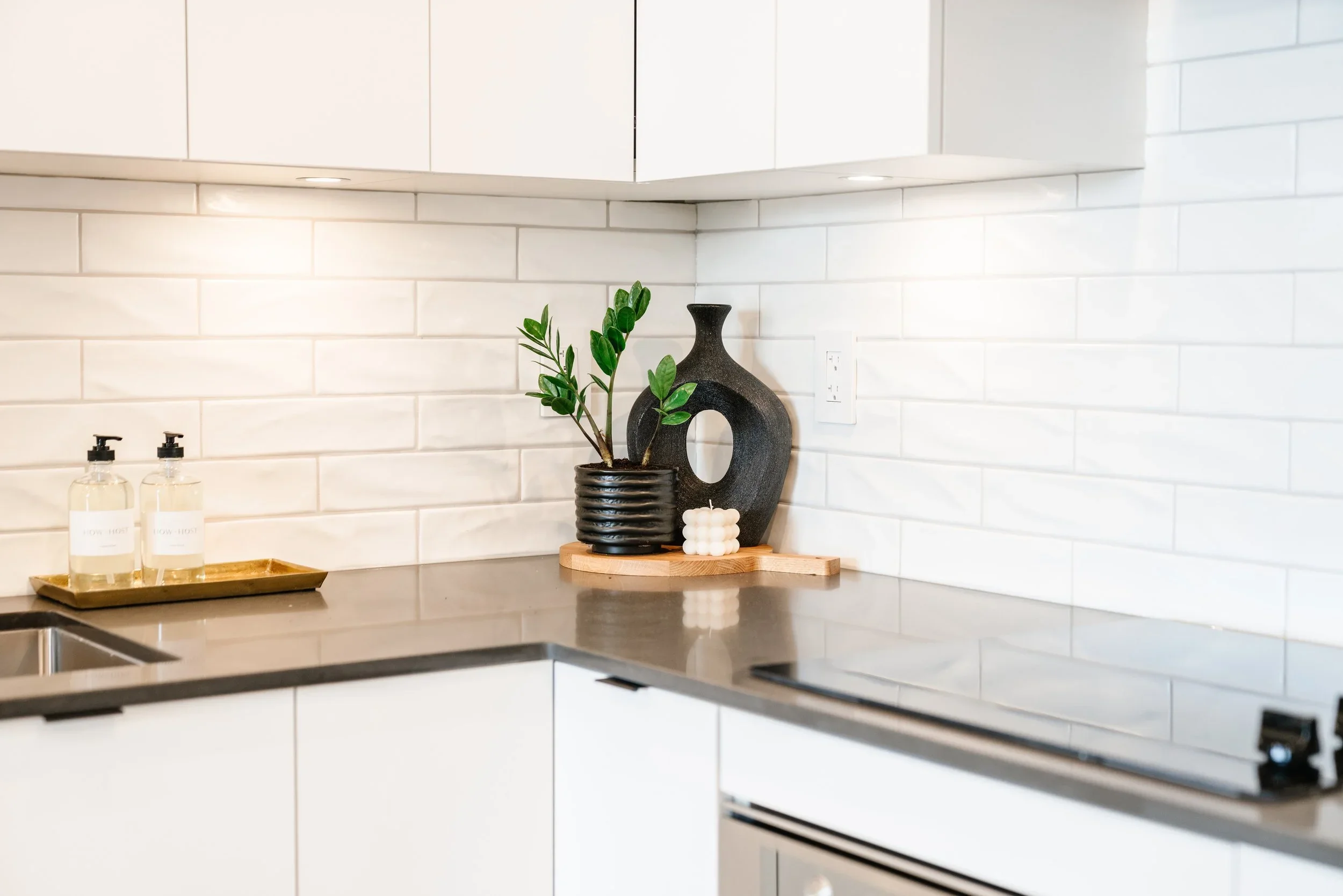Minimalist kitchen corner with white subway tile, organized countertop decor, and a potted plant.