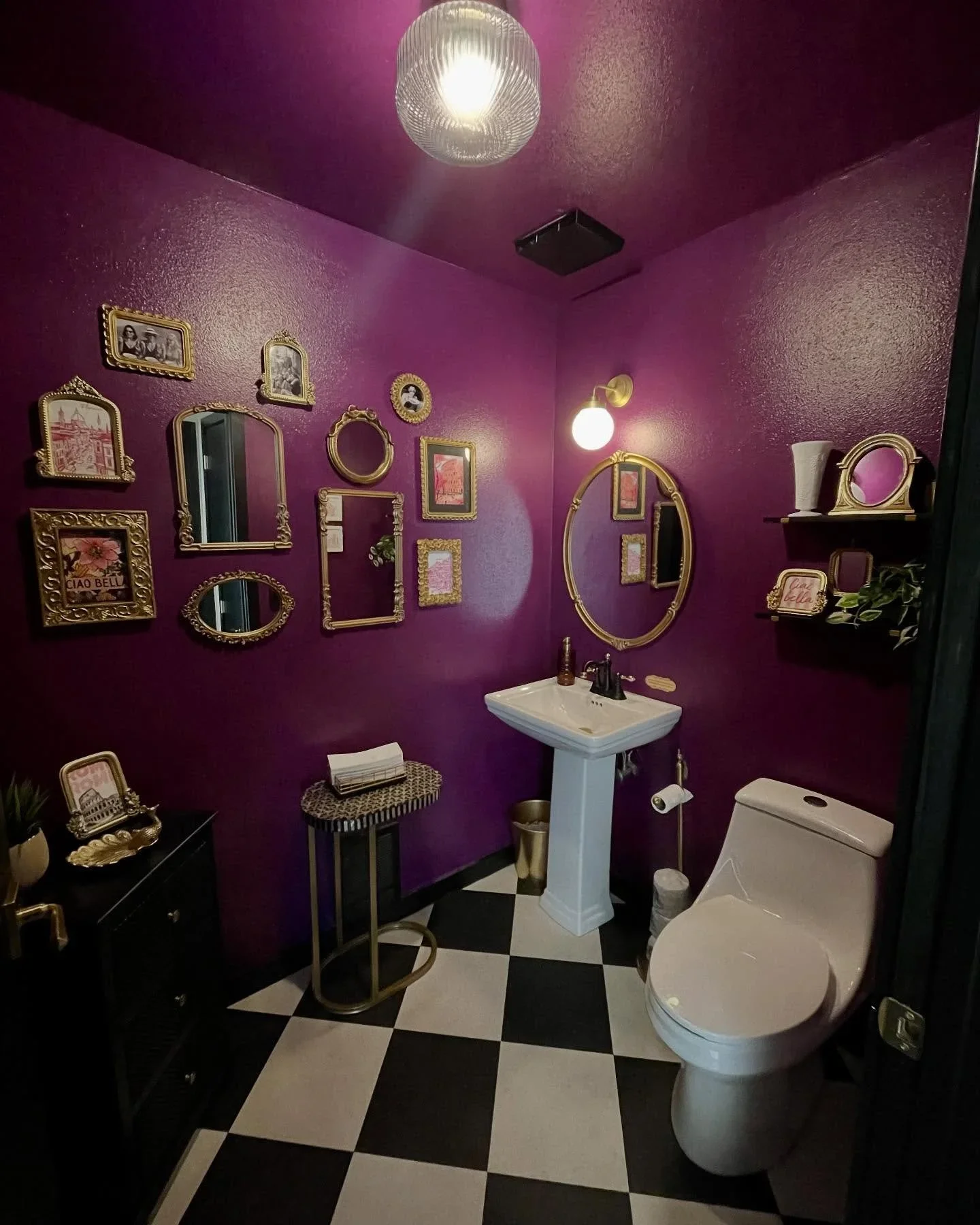 Maximalist purple bathroom by A Neat Day featuring a gold gallery wall and checkered tile floor.
