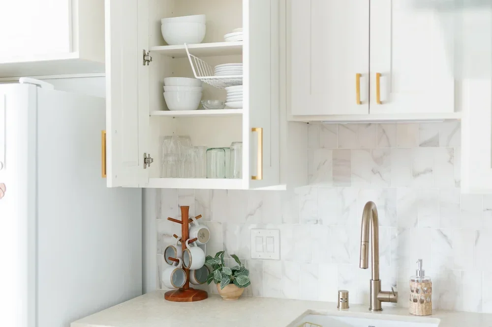 Open white kitchen cabinet with neatly stacked white dishes and organized glassware.