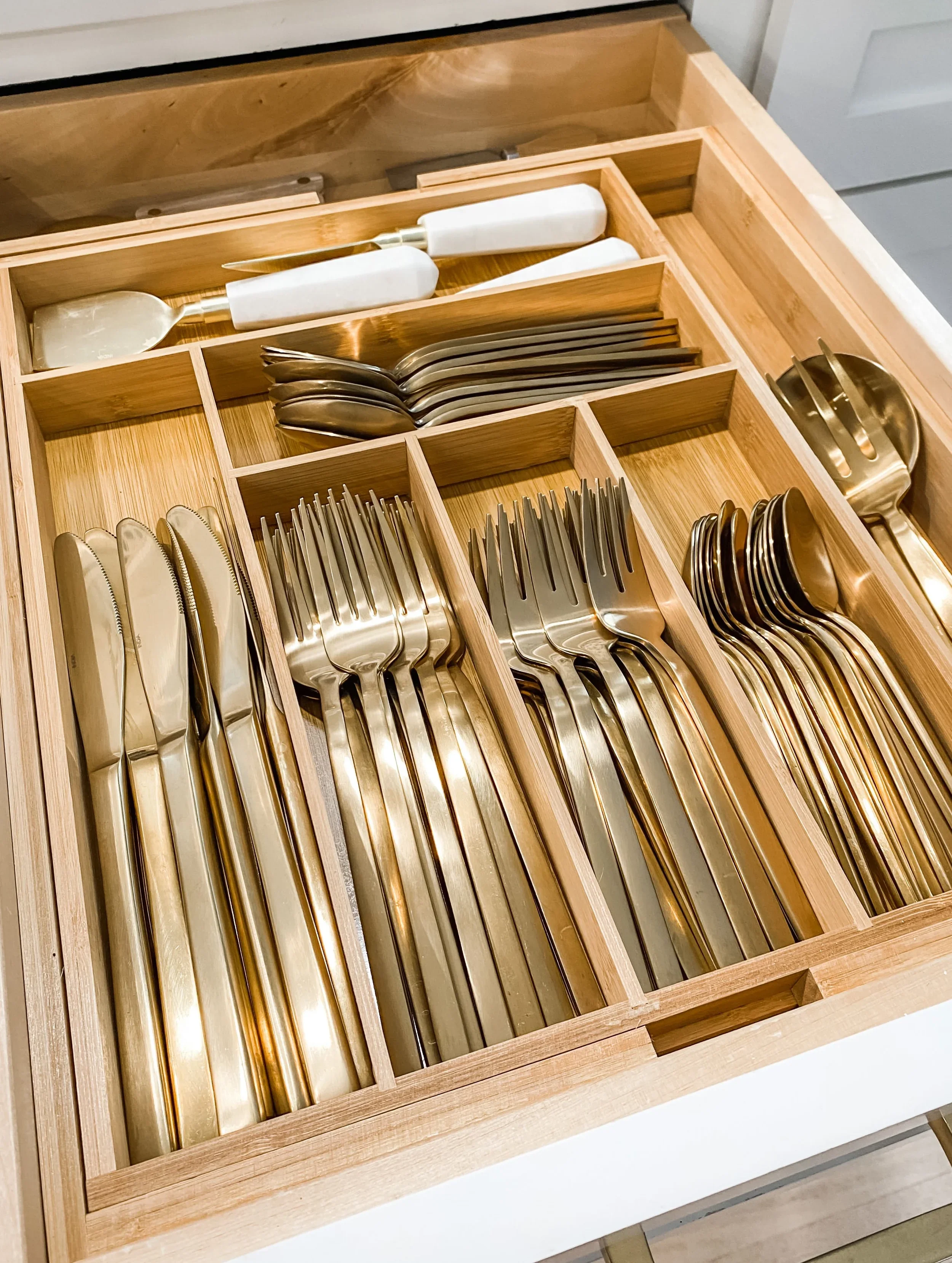 Gold silverware neatly organized in a bamboo drawer divider.