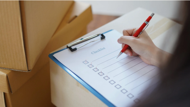 Professional move manager from Organized by Keli & Co. filling out a moving checklist next to cardboard boxes.