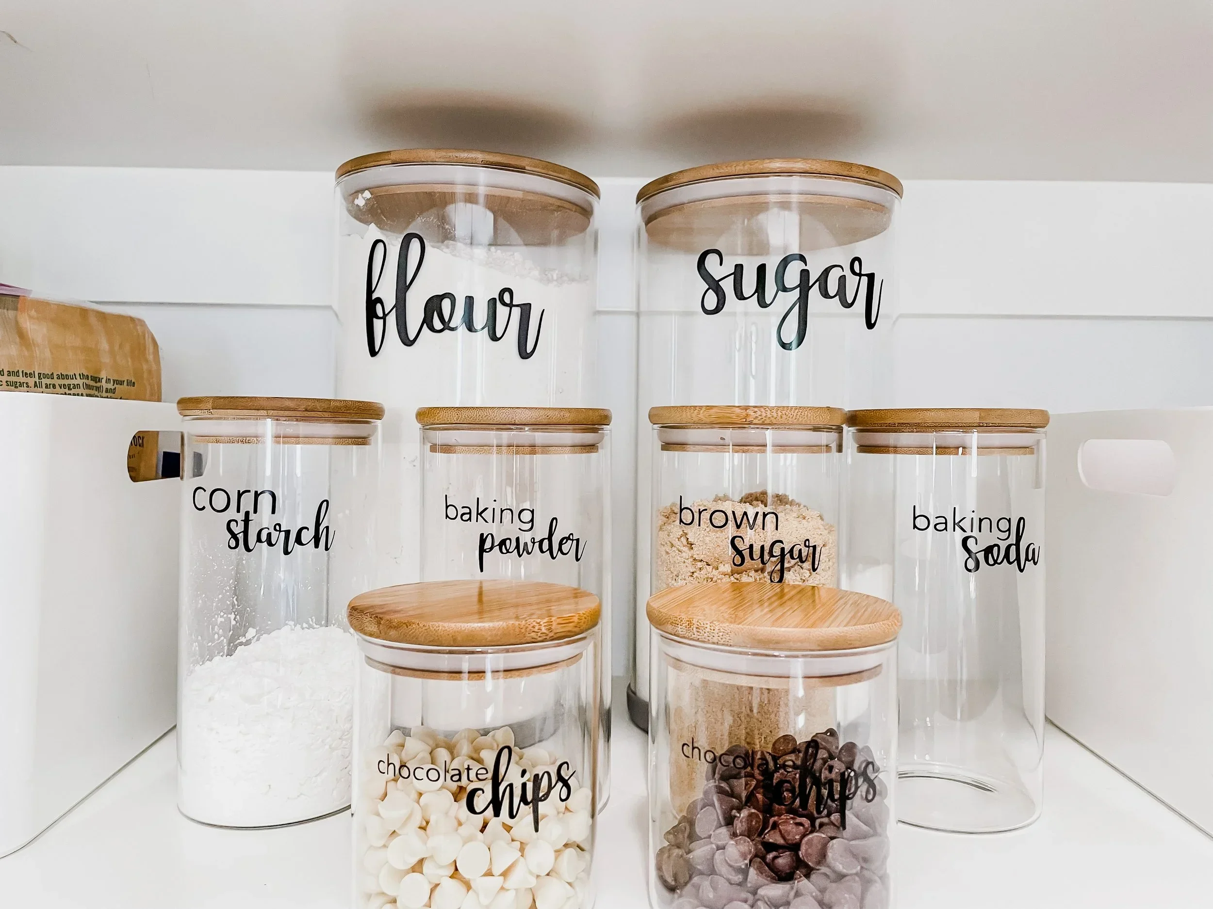 Labeled glass baking jars with bamboo lids for flour, sugar, and chocolate chips, organized by Refined Living Co. in Nashville, TN.