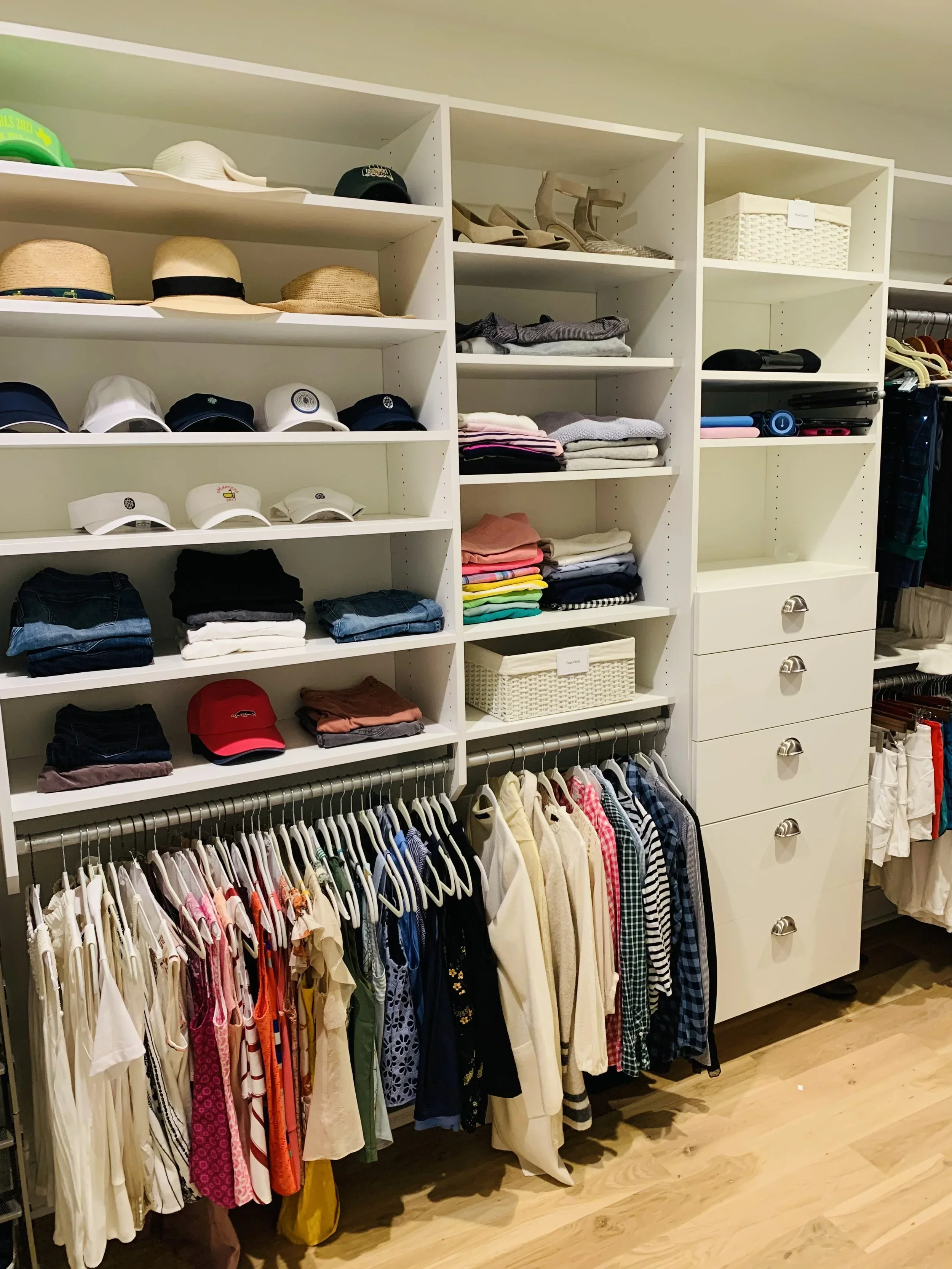 Professional walk-in closet organization by Happy Tree Organizing in Atlanta, featuring white shelving with neatly arranged hats, folded clothes, and hanging garments.