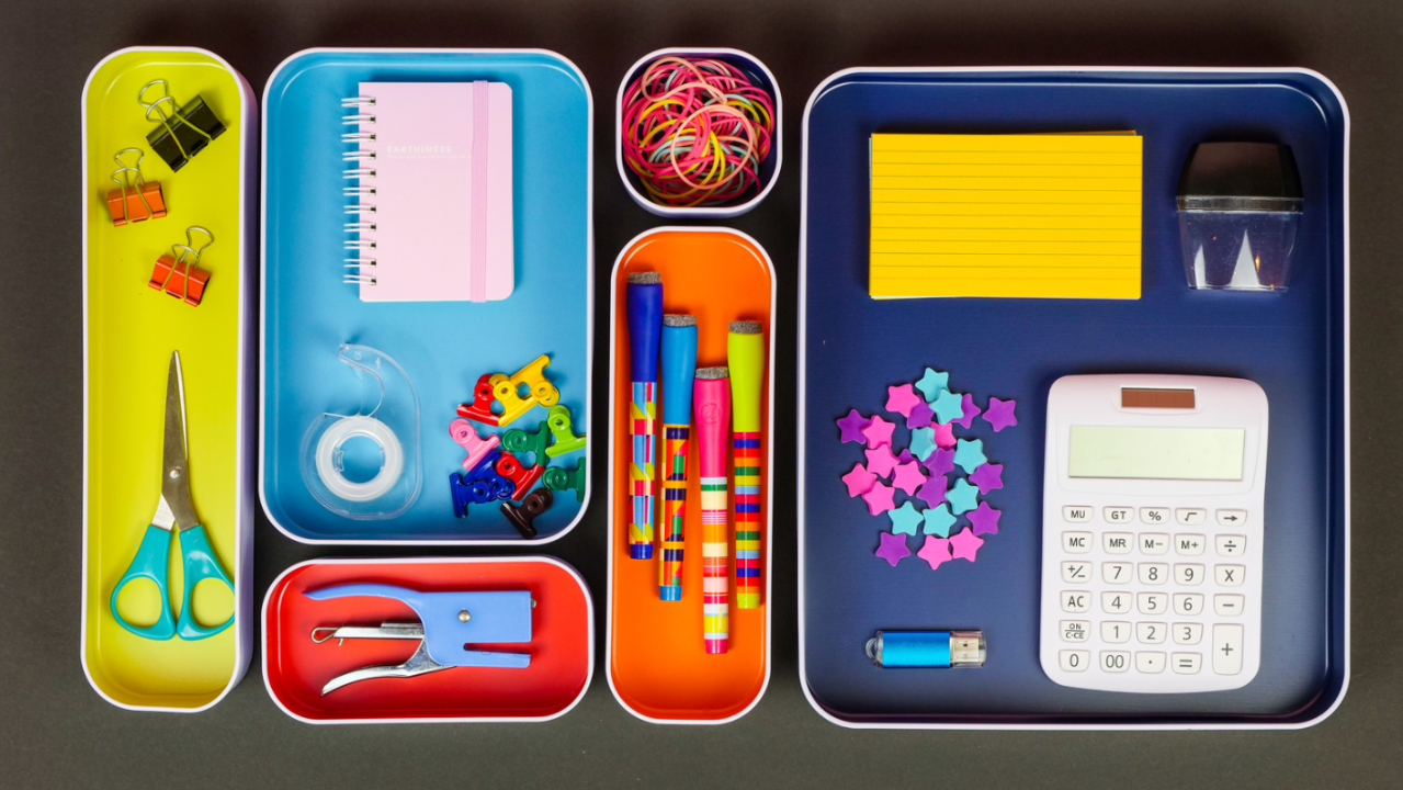 Colorful desk drawer organizers from All In Place Organizing, featuring a calculator, scissors, and stationery in neat trays.
