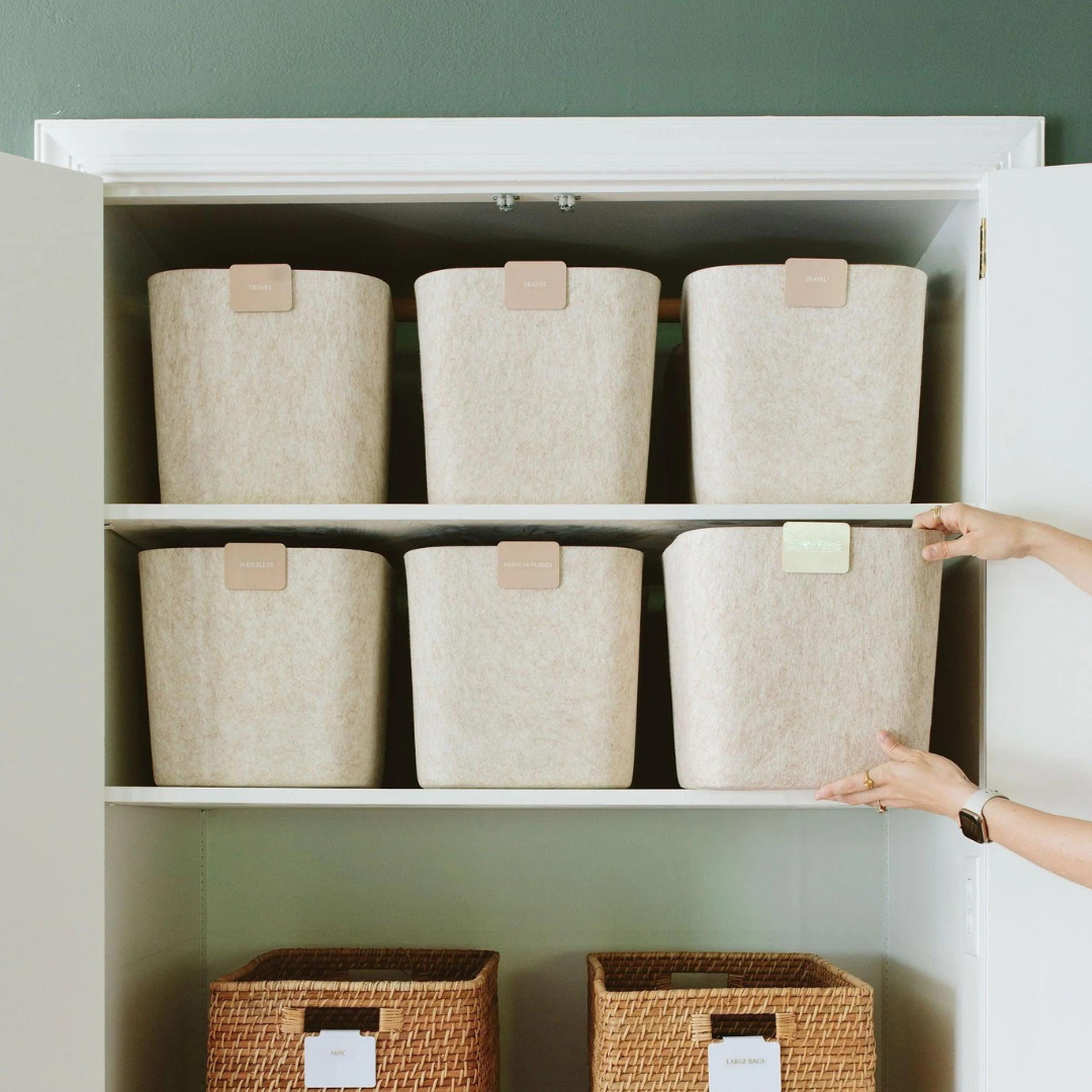 Professional organizer arranging labeled beige SortJoy felt bins in a clean, modern white closet.