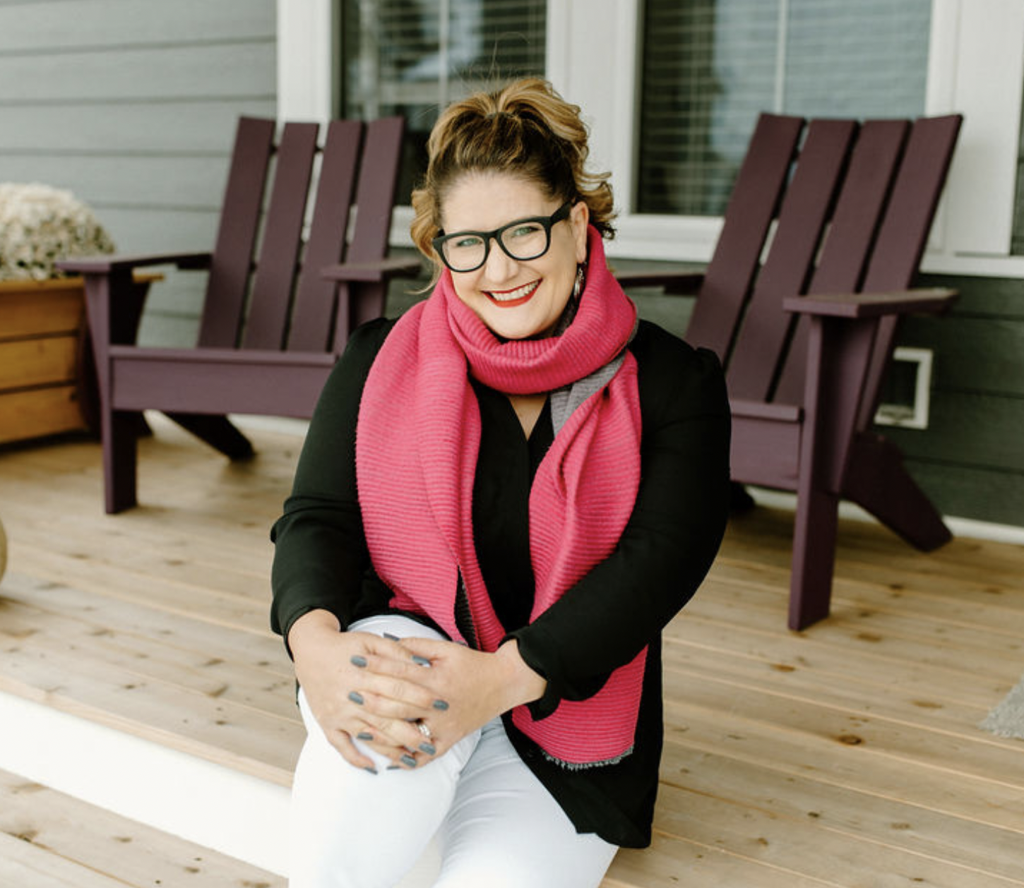 Melissa Klug, owner of Pro Organizer Studio, sitting on an outdoor deck in a bright pink scarf and black top.