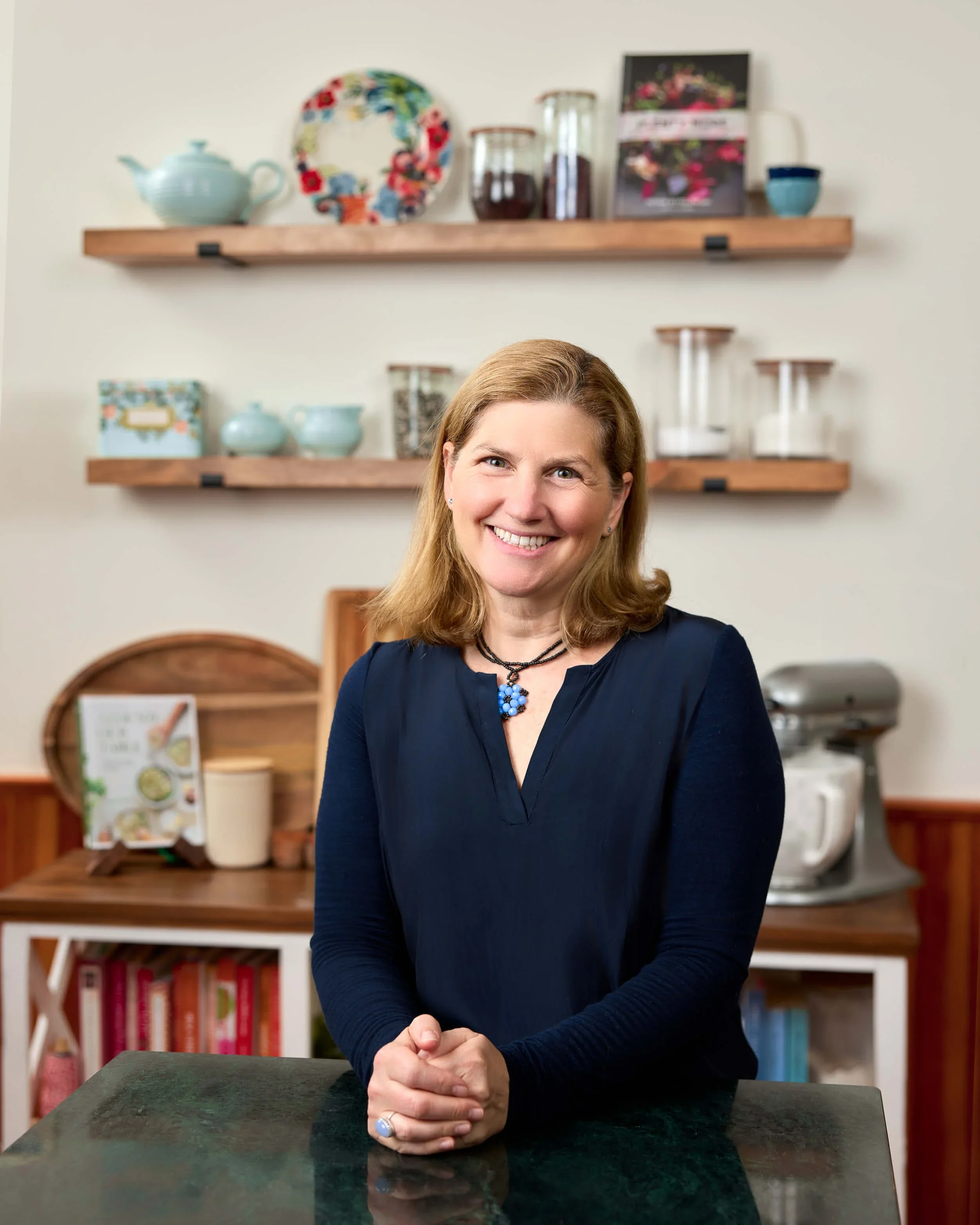 Professional organizer Merrie Deitch, founder of The Tidy Girl, smiling in a kitchen with organized wooden open shelving.