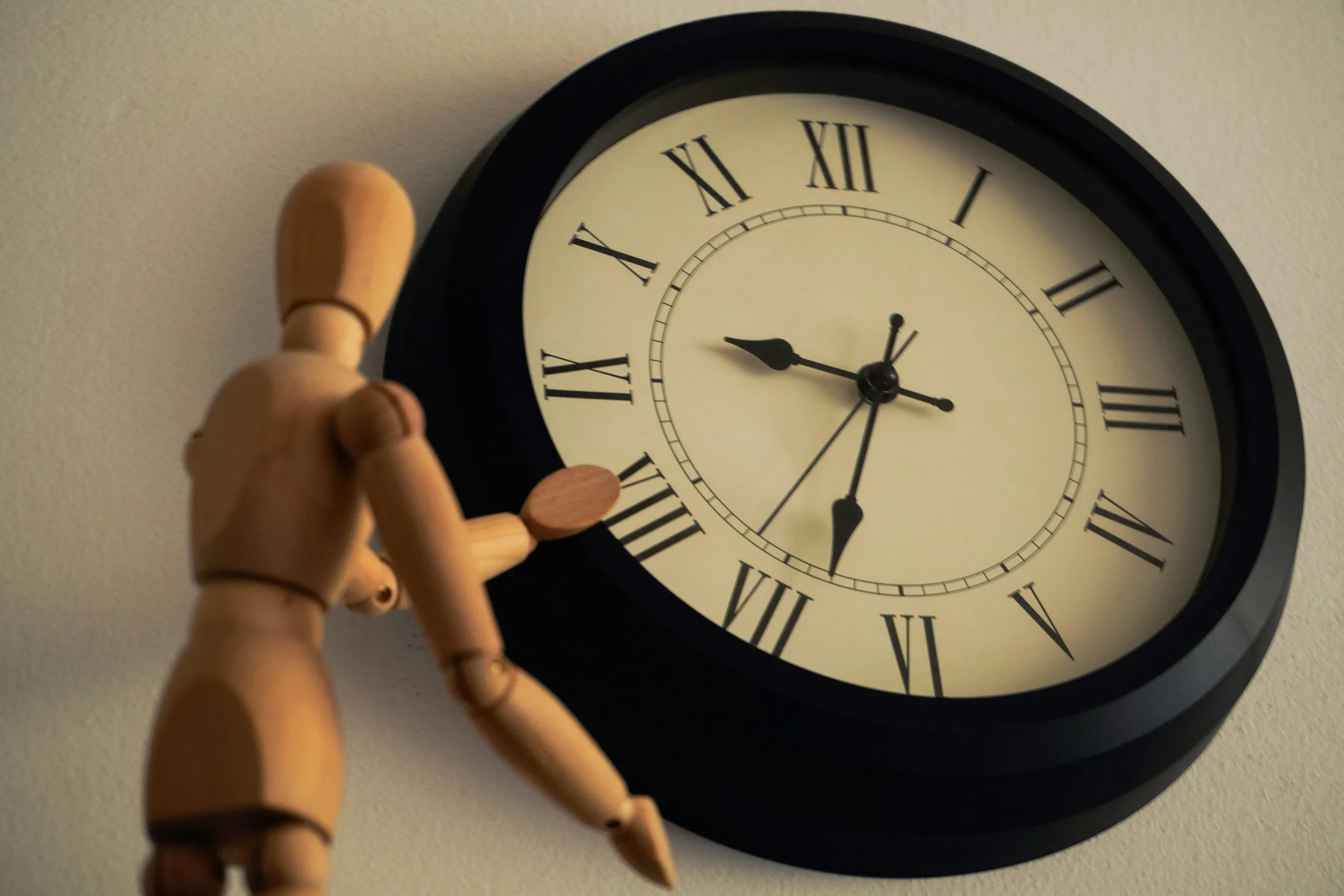 Wooden mannequin reaching for a large black clock, symbolizing time management and organization.