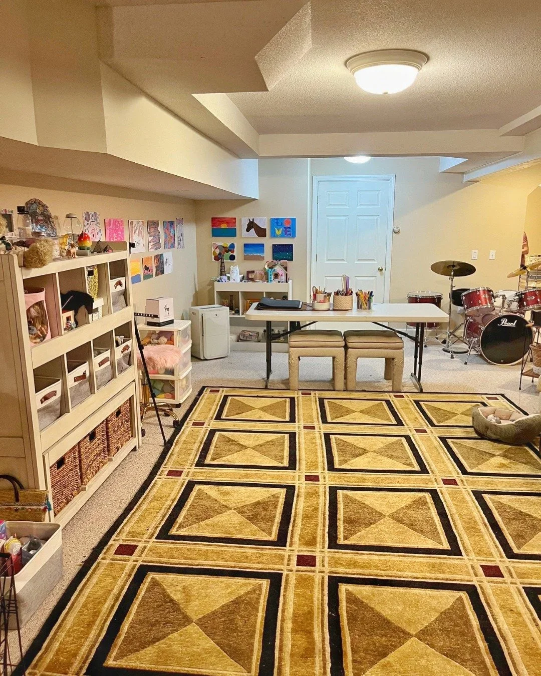 Organized kids' playroom and art studio in Hartford County, CT, by Improved Spaces, featuring white shelving, a craft table, and a drum set.