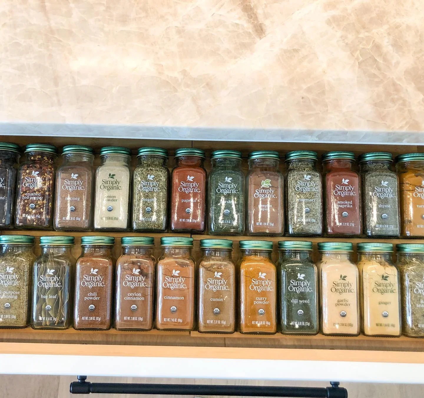 Neatly organized spice drawer in Richmond, VA by Divine Organization, featuring Simply Organic glass jars in tiered rows.