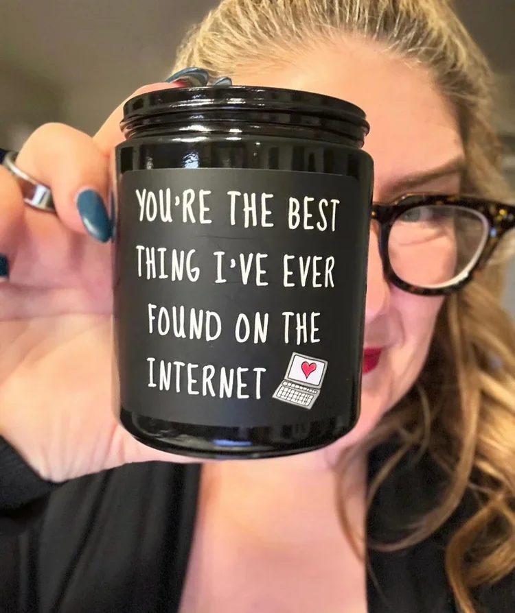 Melissa Klug holding a black candle that says 'You're the best thing I've ever found on the internet.