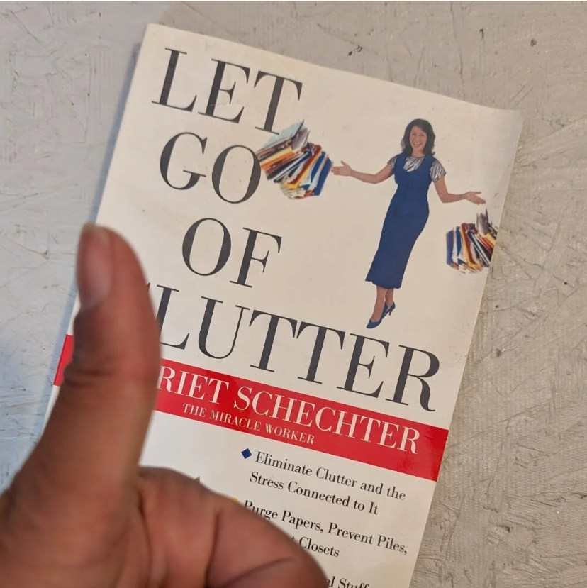 A hand giving a thumbs up in front of Harriet Schechter's book 'Let Go of Clutter,' a resource recommended by Tidy Corners.