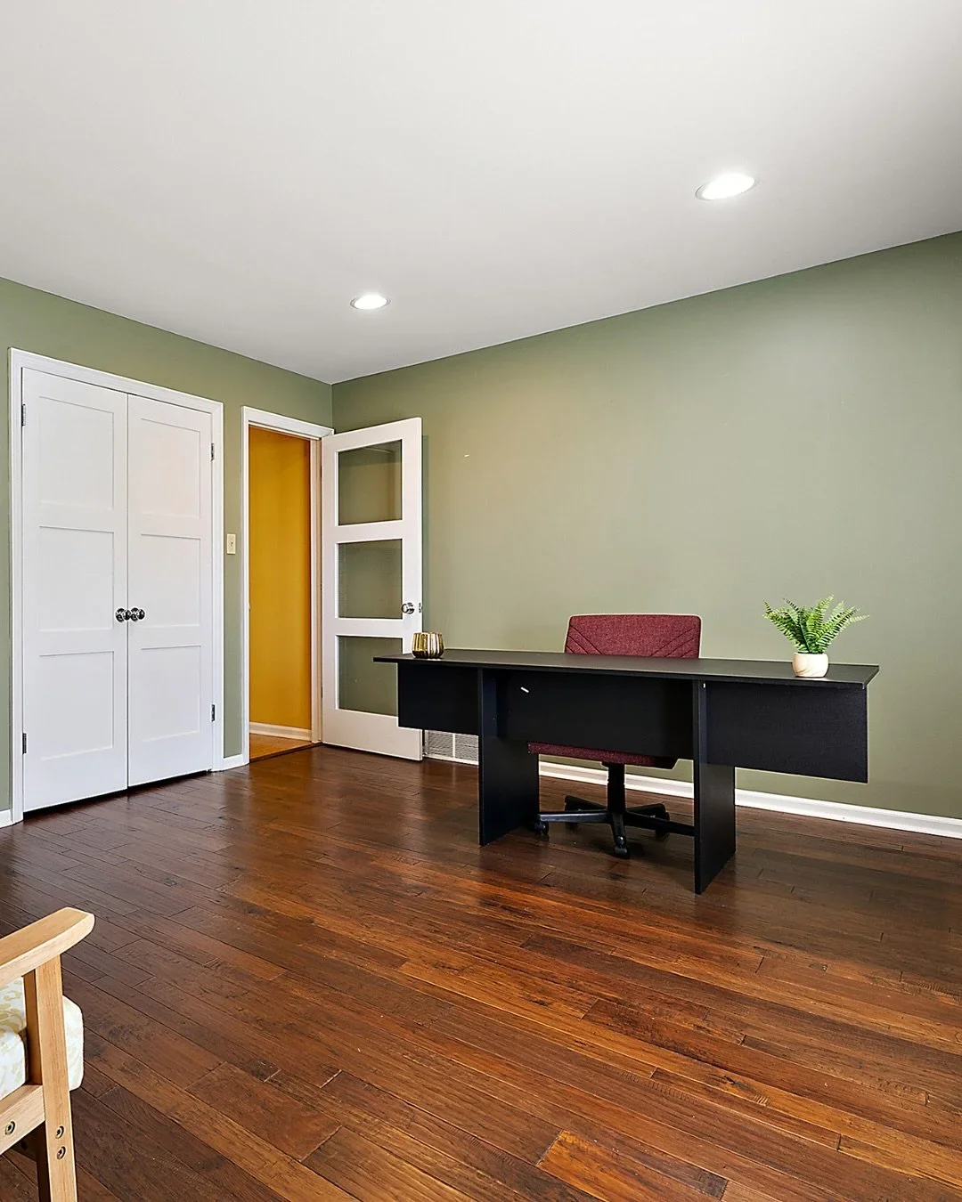 Minimalist organized home office with a black desk, burgundy chair, and sage green walls.