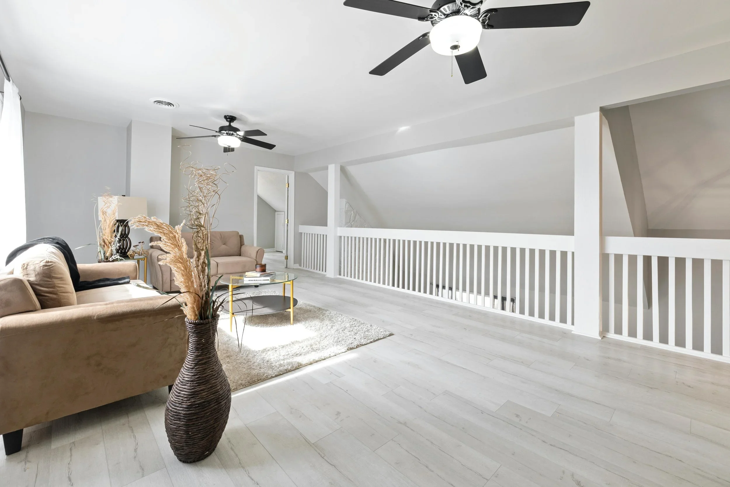 Spacious modern living room with neutral sofas, white railings, and a large decorative vase.