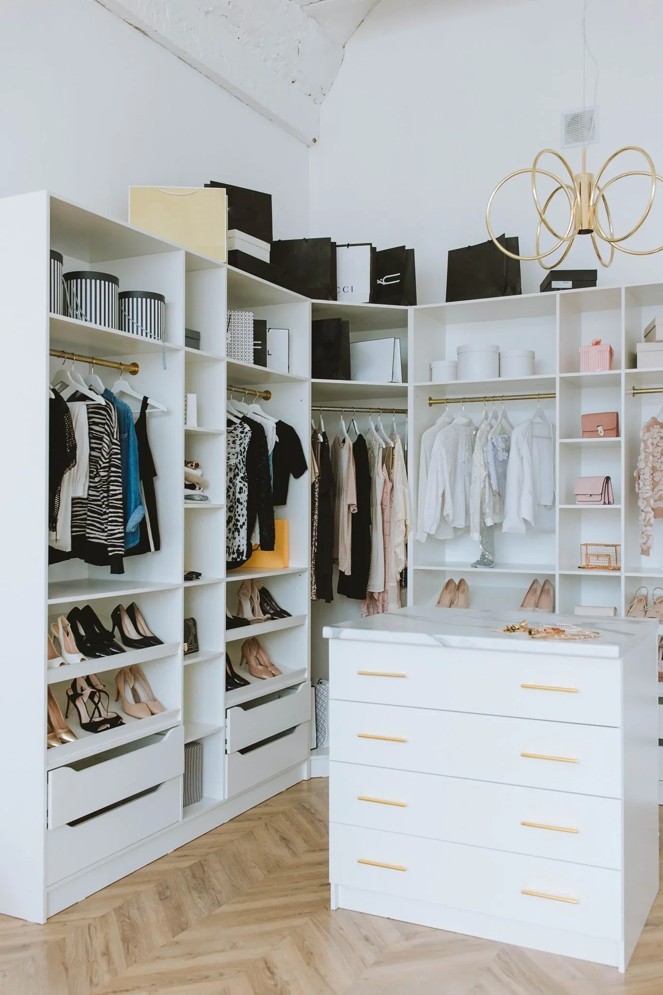 A luxury custom walk-in closet by Organized by Onyee with white shelving, designer bags, and a marble-top island.