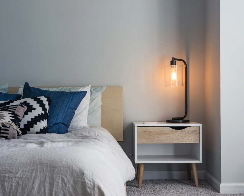 A serene bedroom organized by Julie Aderhold in Green Bay, featuring a minimalist white nightstand with a wood drawer and a glass Edison bulb lamp.