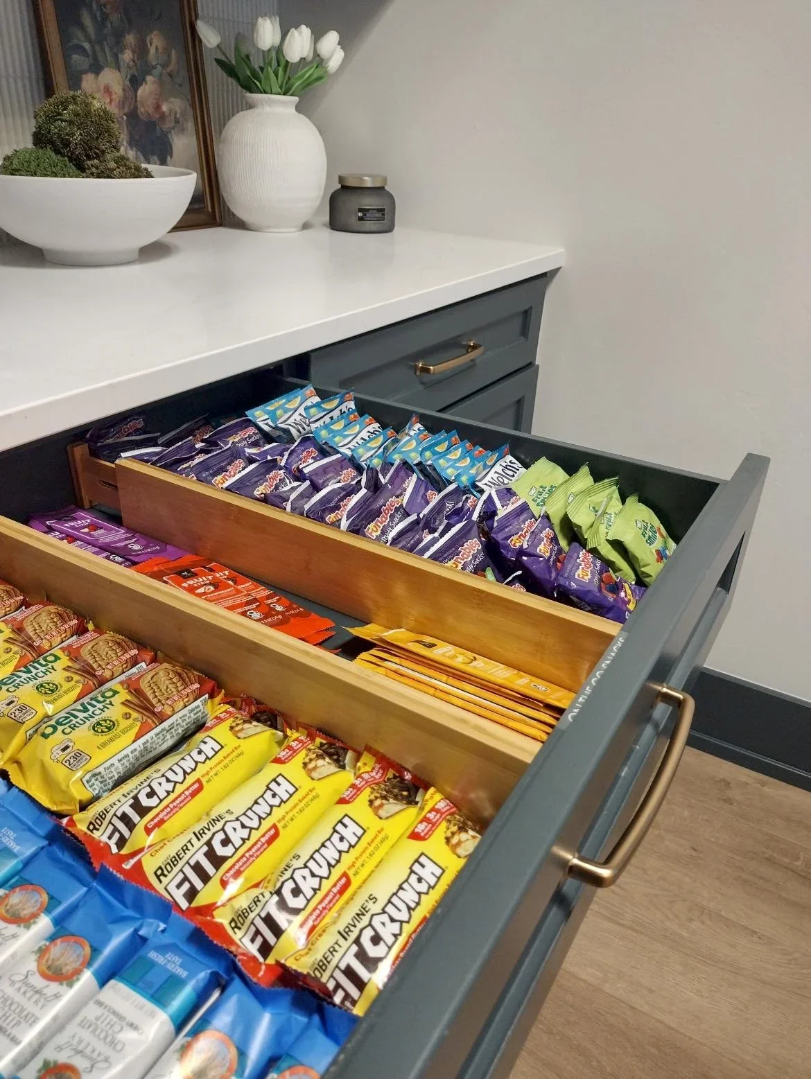A neatly organized kitchen snack drawer by Minimize Then Organize featuring wooden dividers and assorted protein bars.