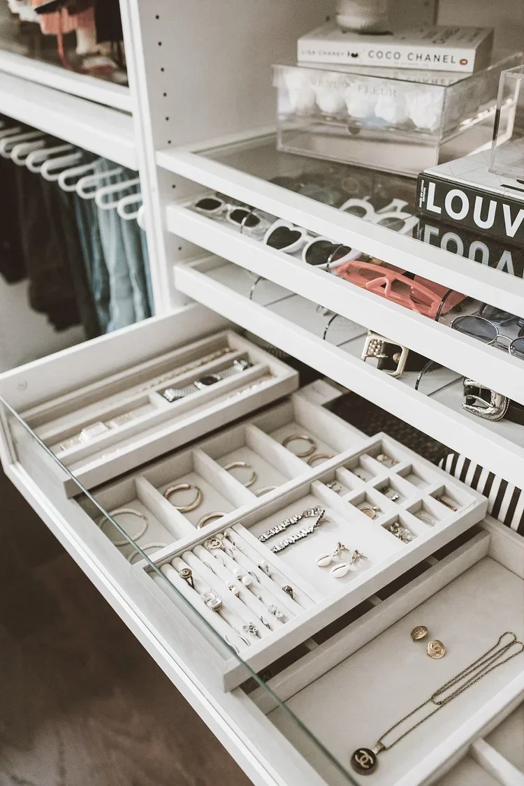 Organized white closet drawer featuring velvet jewelry inserts, gold accessories, and a sunglasses display.