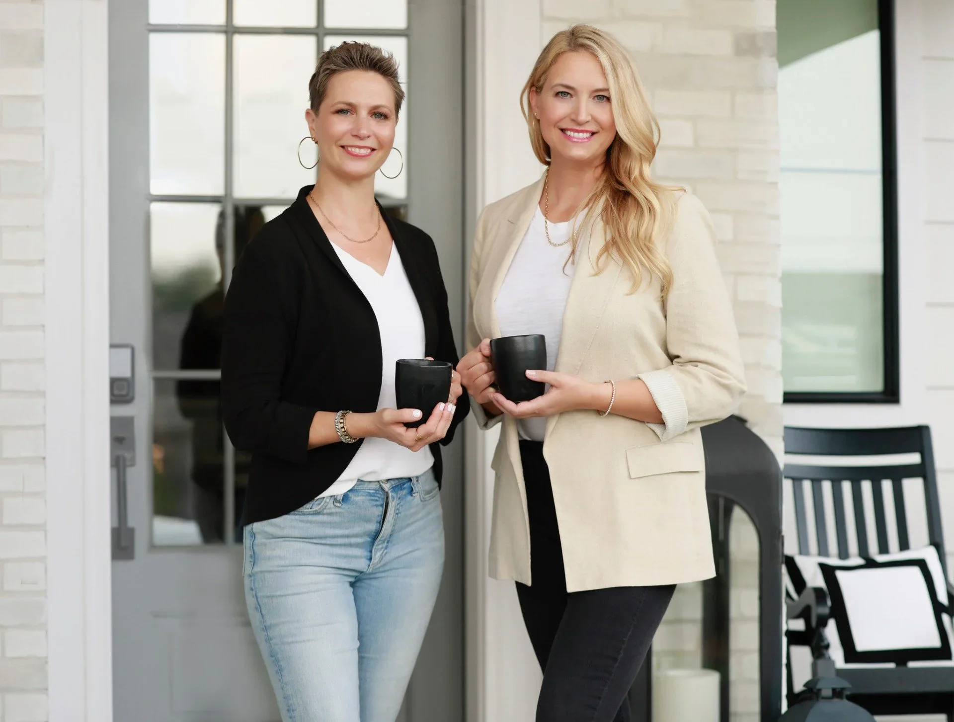 Professional organizers from We Organize smiling and holding black coffee mugs on a porch.