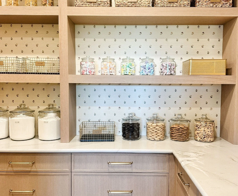 Professional pantry organization by Reset Your Nest in Utah, featuring labeled glass jars and wire bins on light wood shelves with patterned wallpaper.