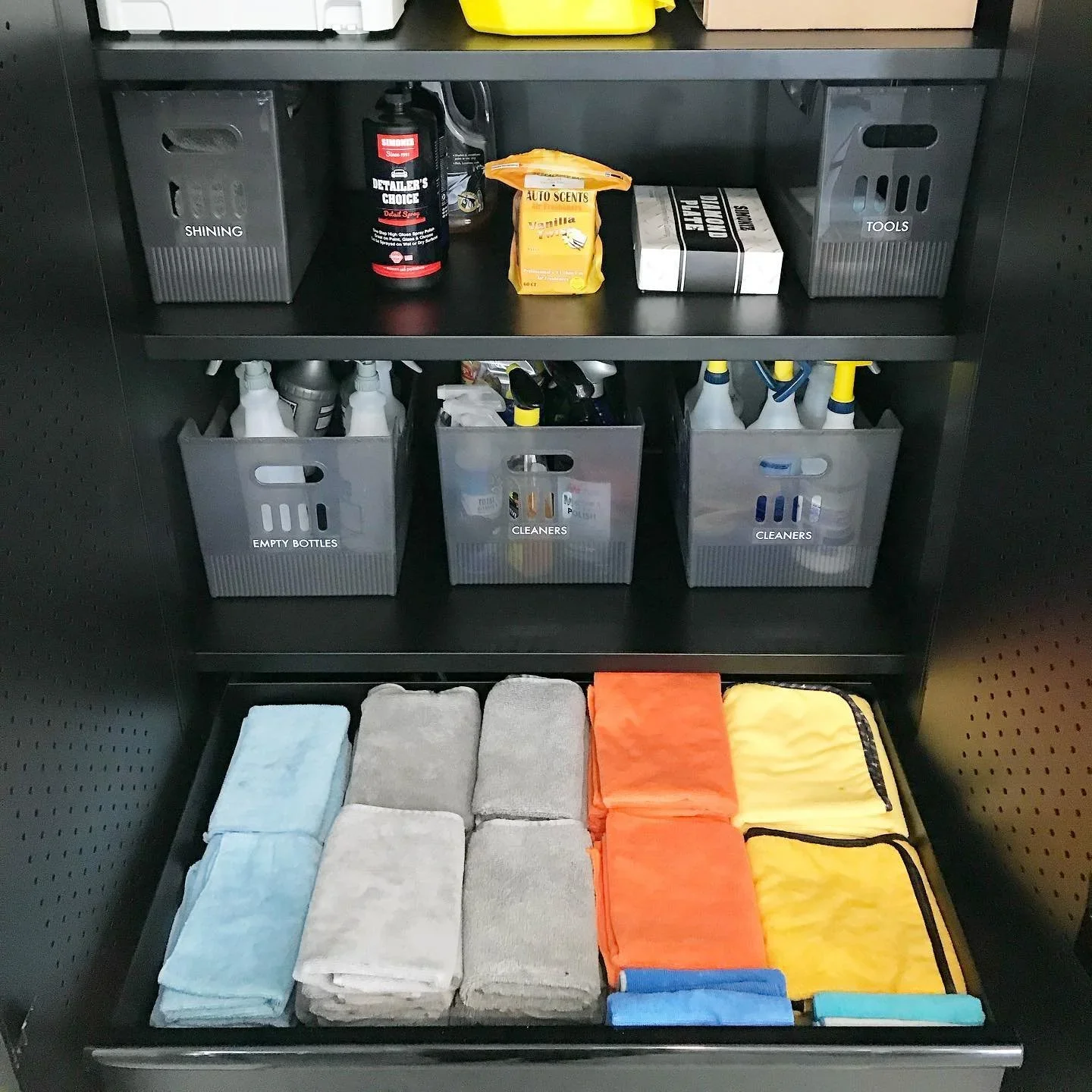 Professional garage storage by Practical Harmony in Bloomington, IL, featuring labeled bins for cleaners and tools with neatly folded microfiber towels.