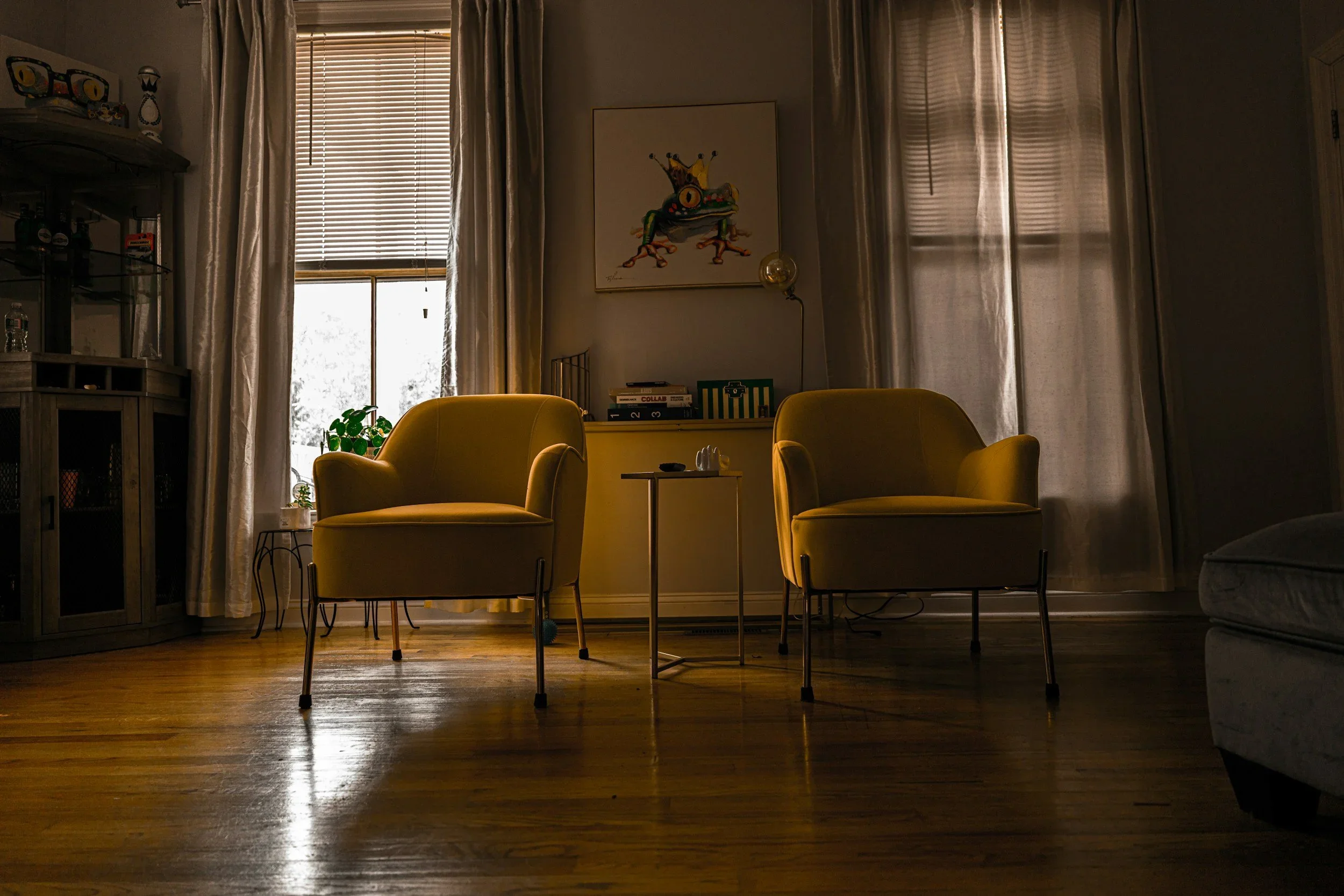 Two symmetrical yellow armchairs in a dimly lit, balanced living room with wood floors.
