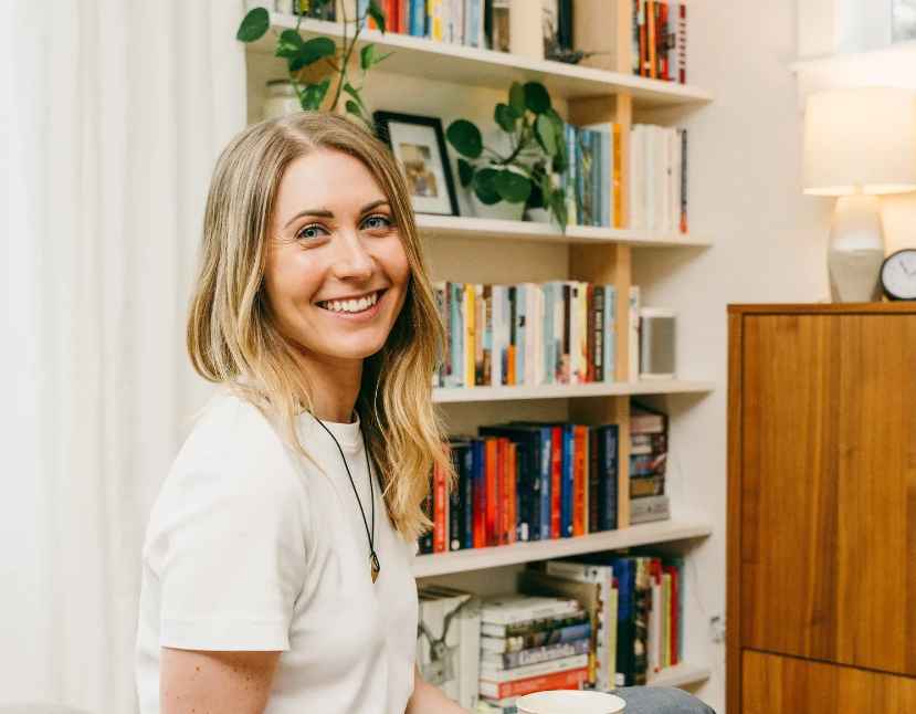 Professional organizer Kari Lonczak, founder of Refine Organizing, smiling in a white t-shirt in front of a neatly organized bookshelf in Seattle, WA.