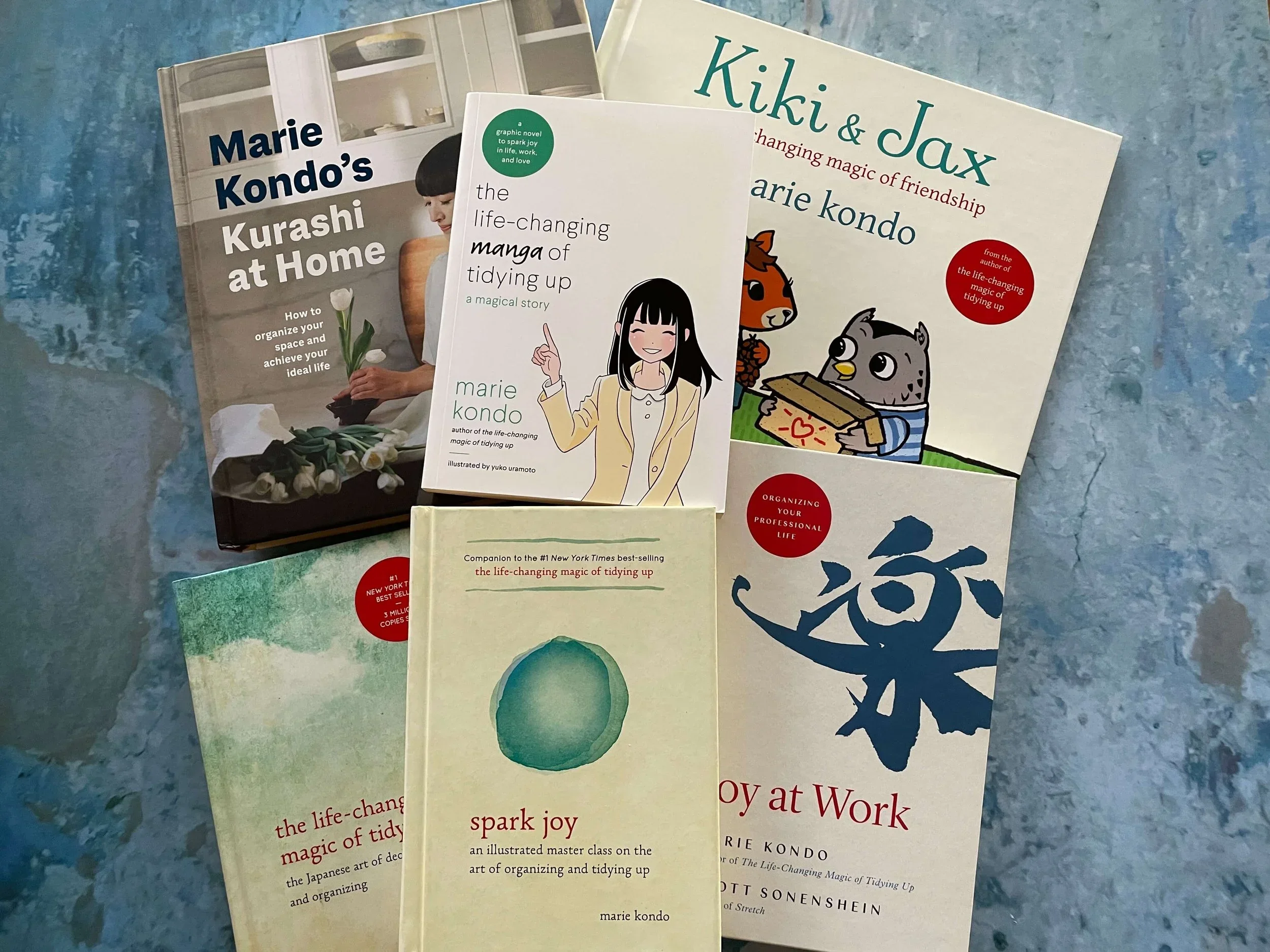 A collection of Marie Kondo books including Spark Joy and Joy at Work on a blue background.