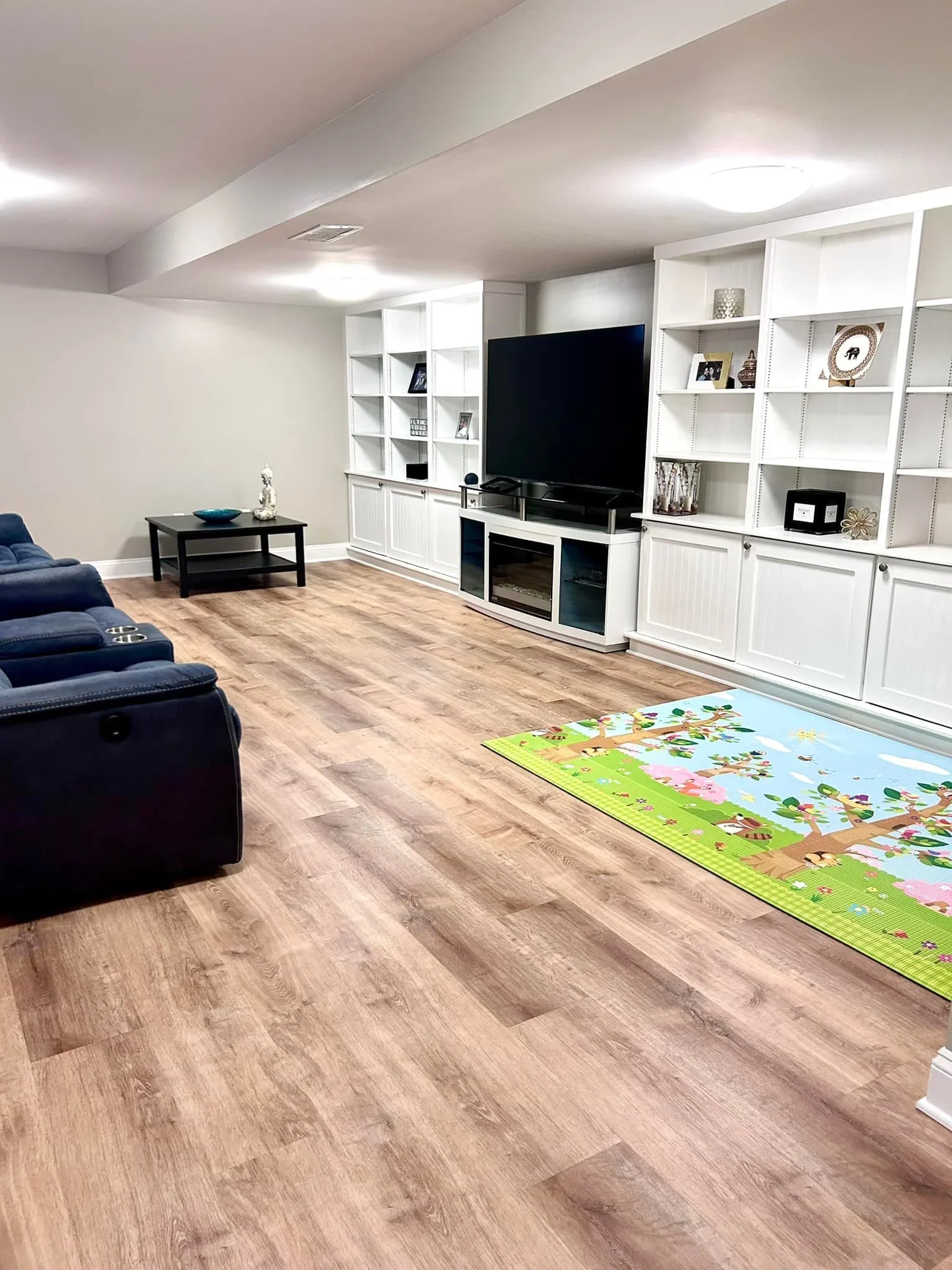 An organized basement family room and playroom in Upstate NY by Peaceful Priorities Organizing, featuring white built-in shelving and blue seating.