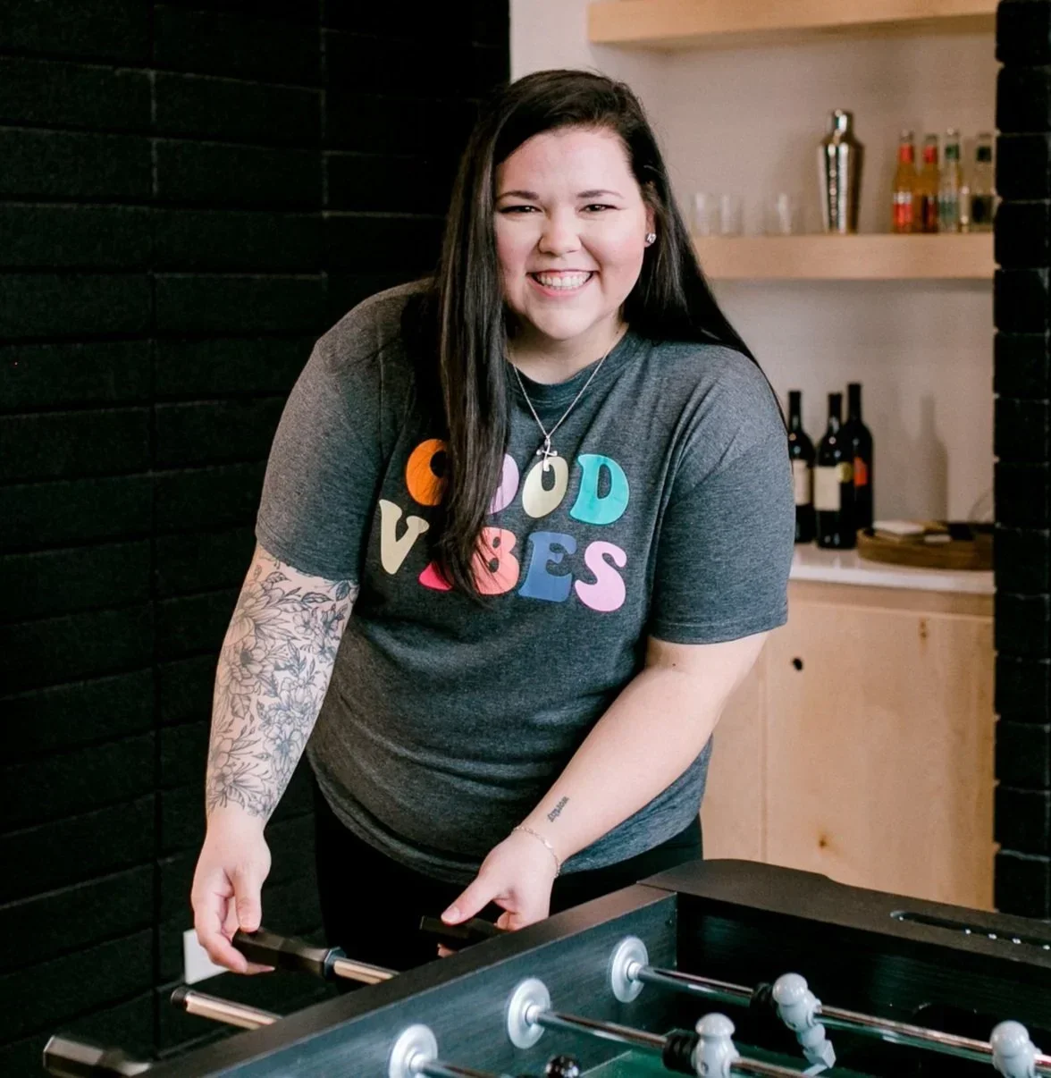 Professional organizer Cabri Caldwell smiling in a Good Vibes shirt while playing foosball.