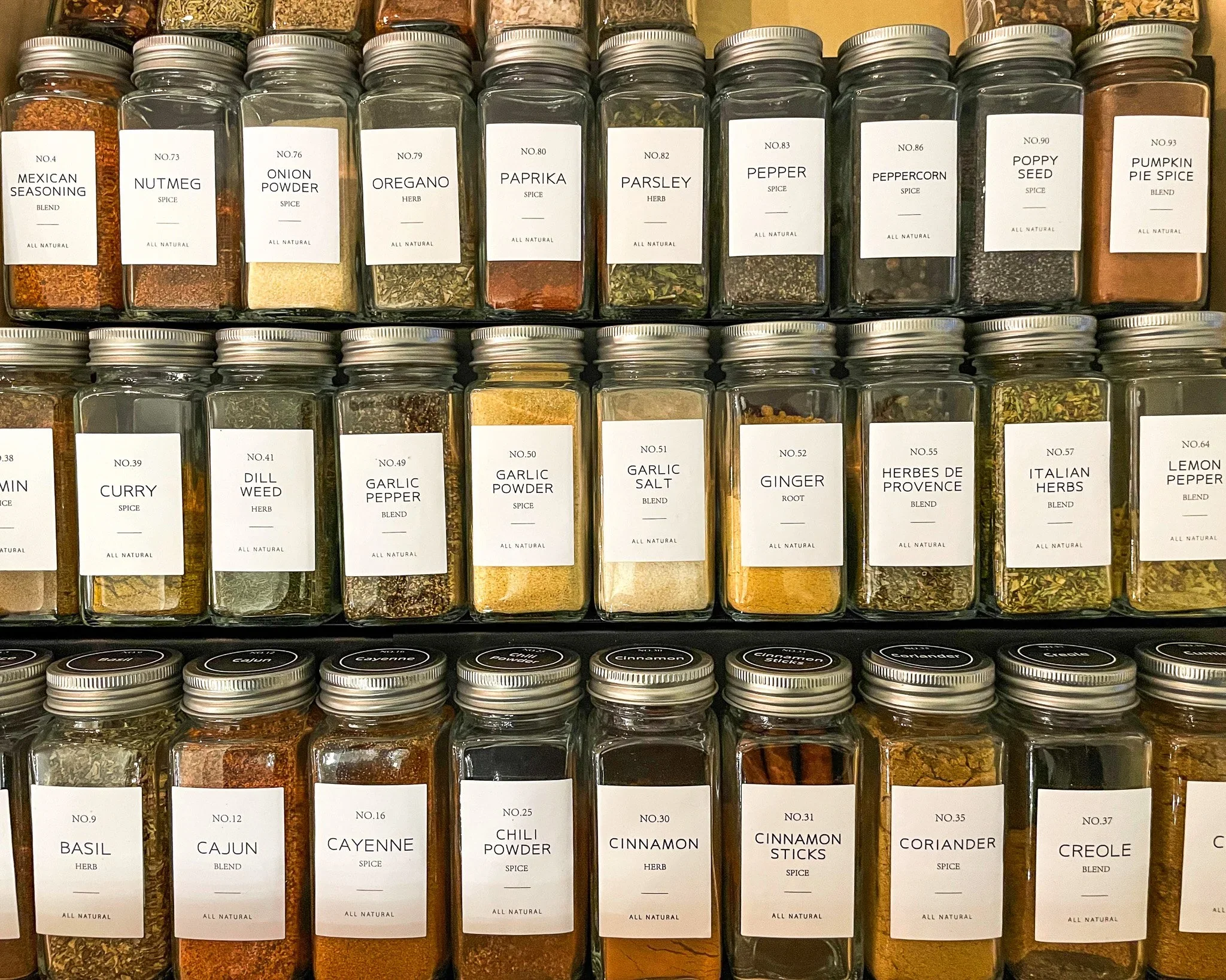 Uniform glass spice jars with minimalist white labels neatly arranged in a pantry.