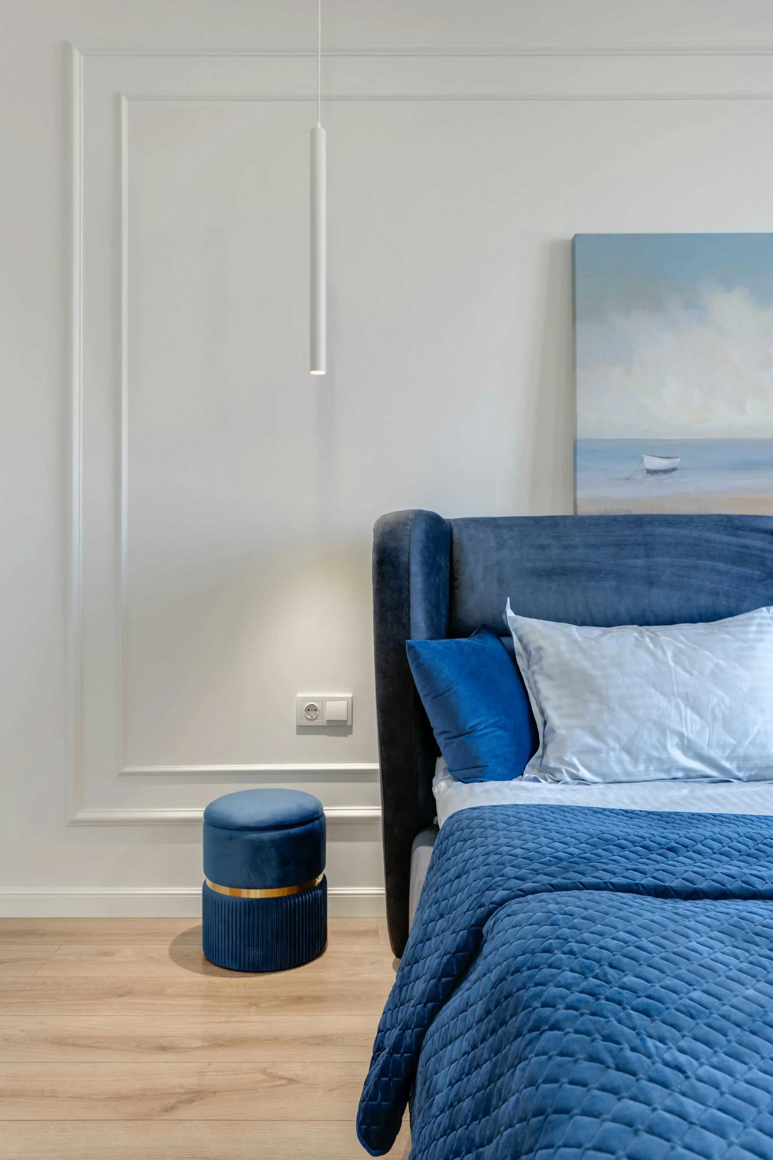 A serene bedroom organized by The Tidy Girl in Boston, featuring deep blue quilted bedding and a modern velvet ottoman.