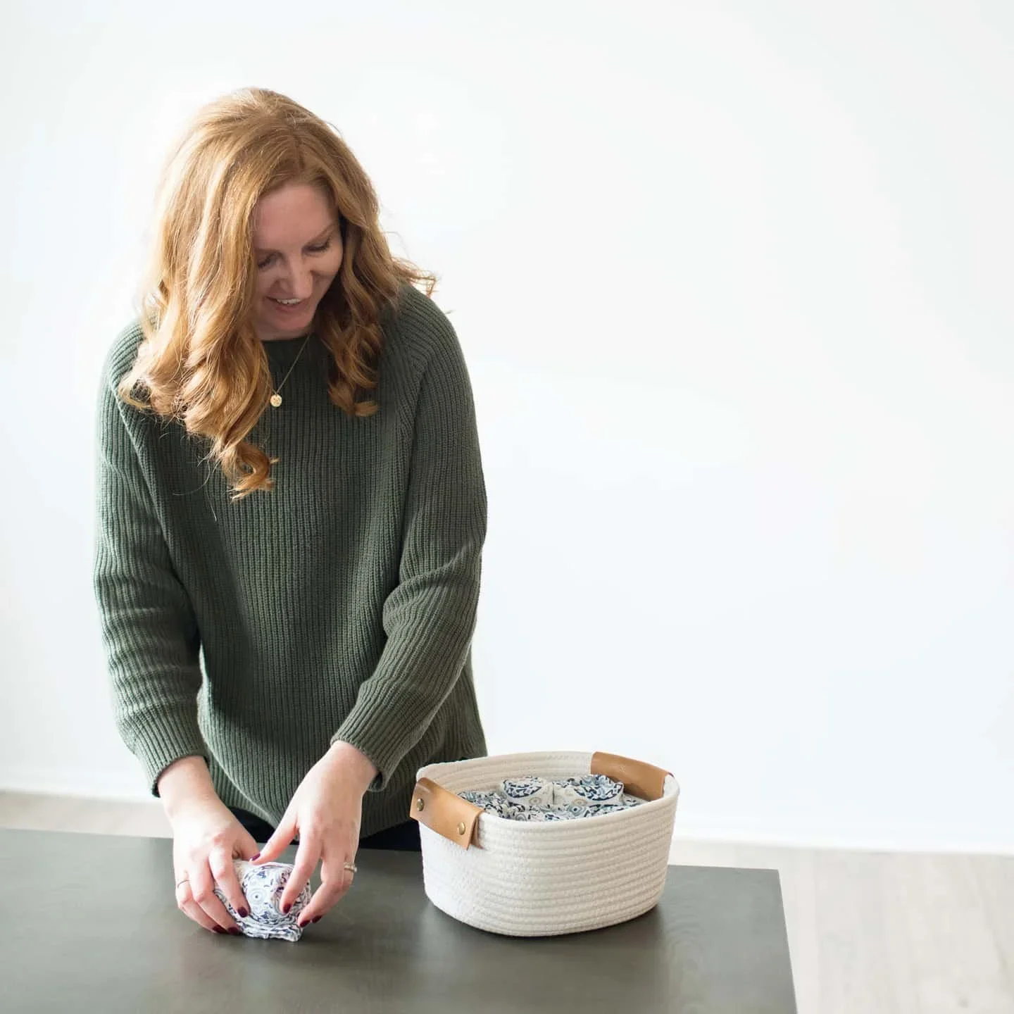 Professional organizer from Creating Clear Spaces folding blue patterned linens into a white woven storage basket.