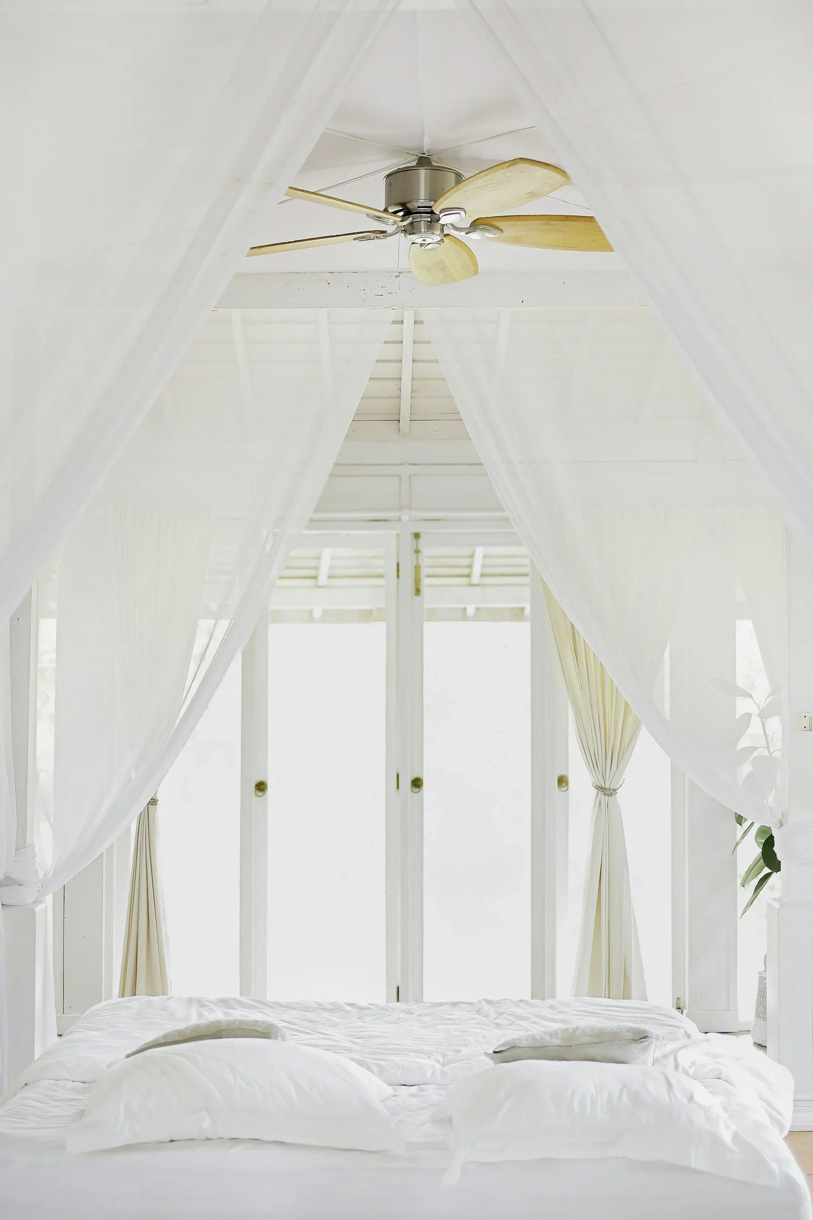 A bright, serene white bedroom with a canopy bed and wooden ceiling fan, styled by Sweet Spaces home organizing in New Jersey.