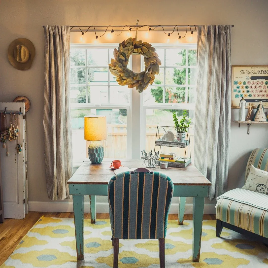 A bright, eclectic home office desk with a teal striped chair, a yellow lamp, and a natural leaf wreath hanging in the window by Sugar & Space.