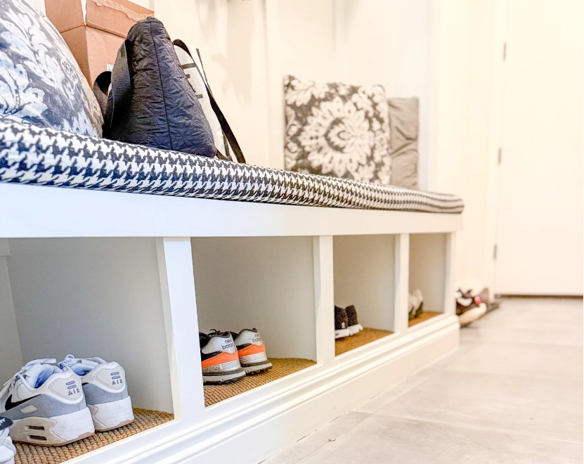 Professional mudroom shoe organization by Serenity at Home in Rochester, MI, featuring a white built-in bench with shoe cubbies and patterned cushions.